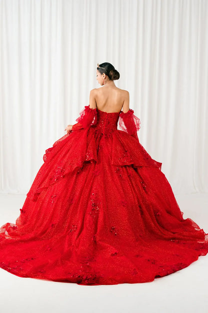Full back view of a woman wearing red quinceañera dress with voluminous glitter tulle skirt, lace-up corset closure, and floral applique embellishments.
