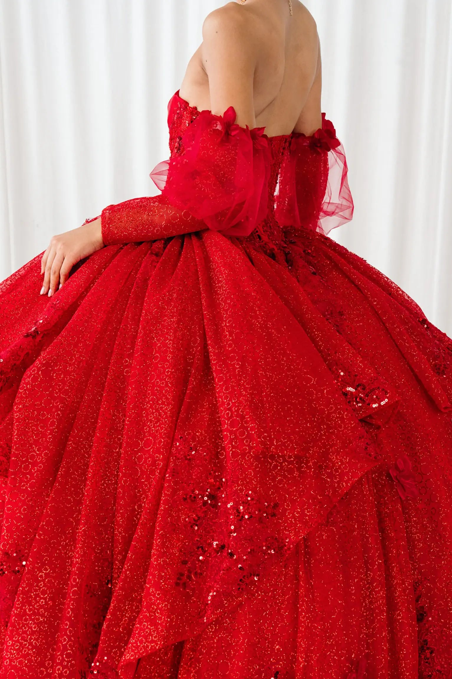 Side close-up view of a red quinceañera dress highlighting detachable tulle sleeves, floral bodice details, and layered glitter tulle skirt.