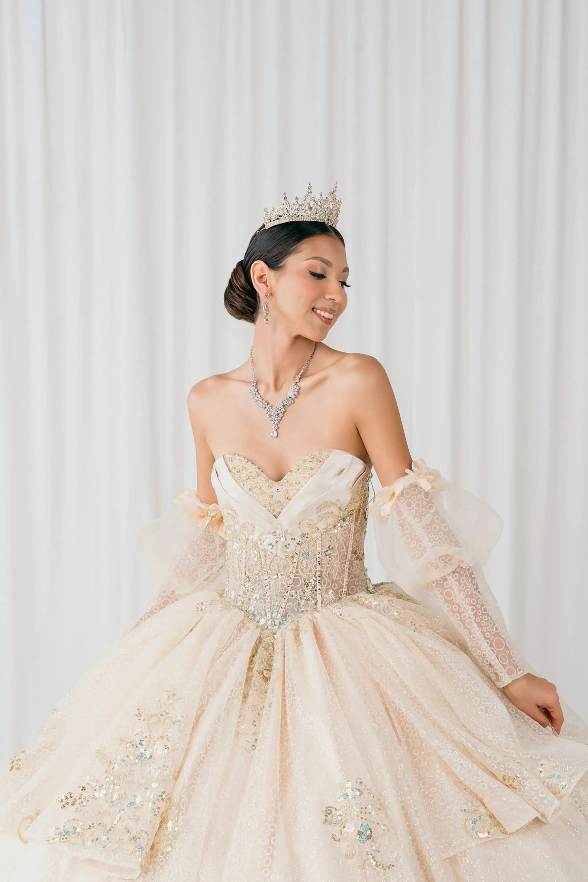Front full-length view of Champagne quinceañera ball gown with off shoulder tulle sleeves, sweetheart sequin bodice, layered glitter tulle skirt, and cathedral train