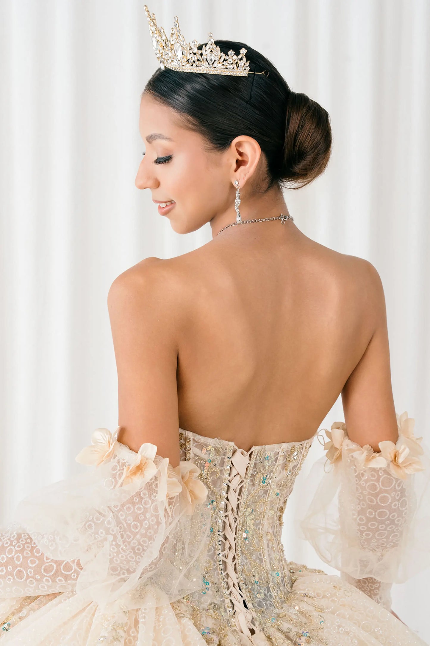 Back close-up Champagne quinceañera ball gown with off shoulder tulle sleeves, sweetheart sequin bodice, layered glitter tulle skirt, and cathedral train