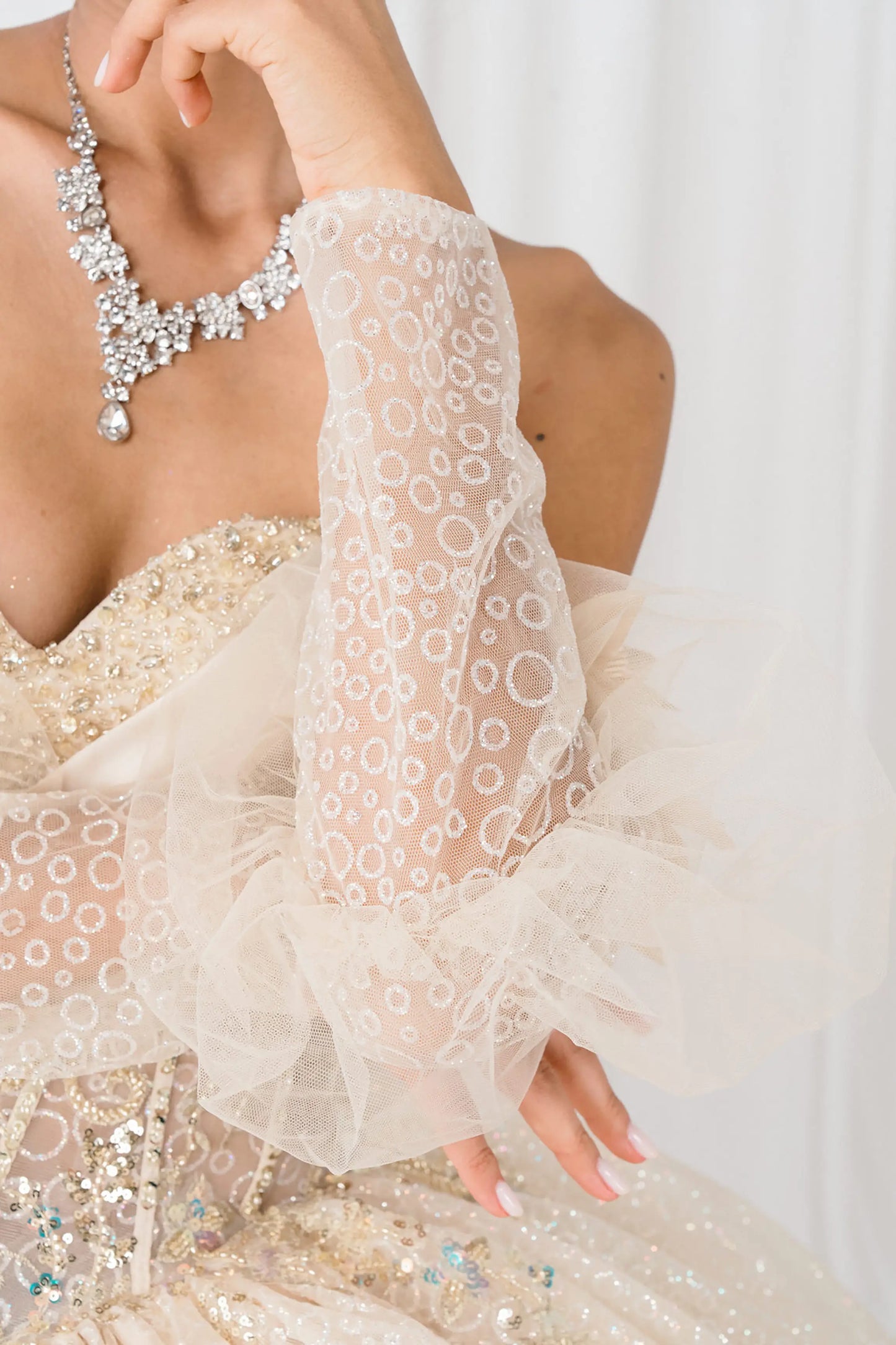 Front half close-up Champagne quinceañera ball gown with off shoulder tulle sleeves, sweetheart sequin bodice, layered glitter tulle skirt, and cathedral train