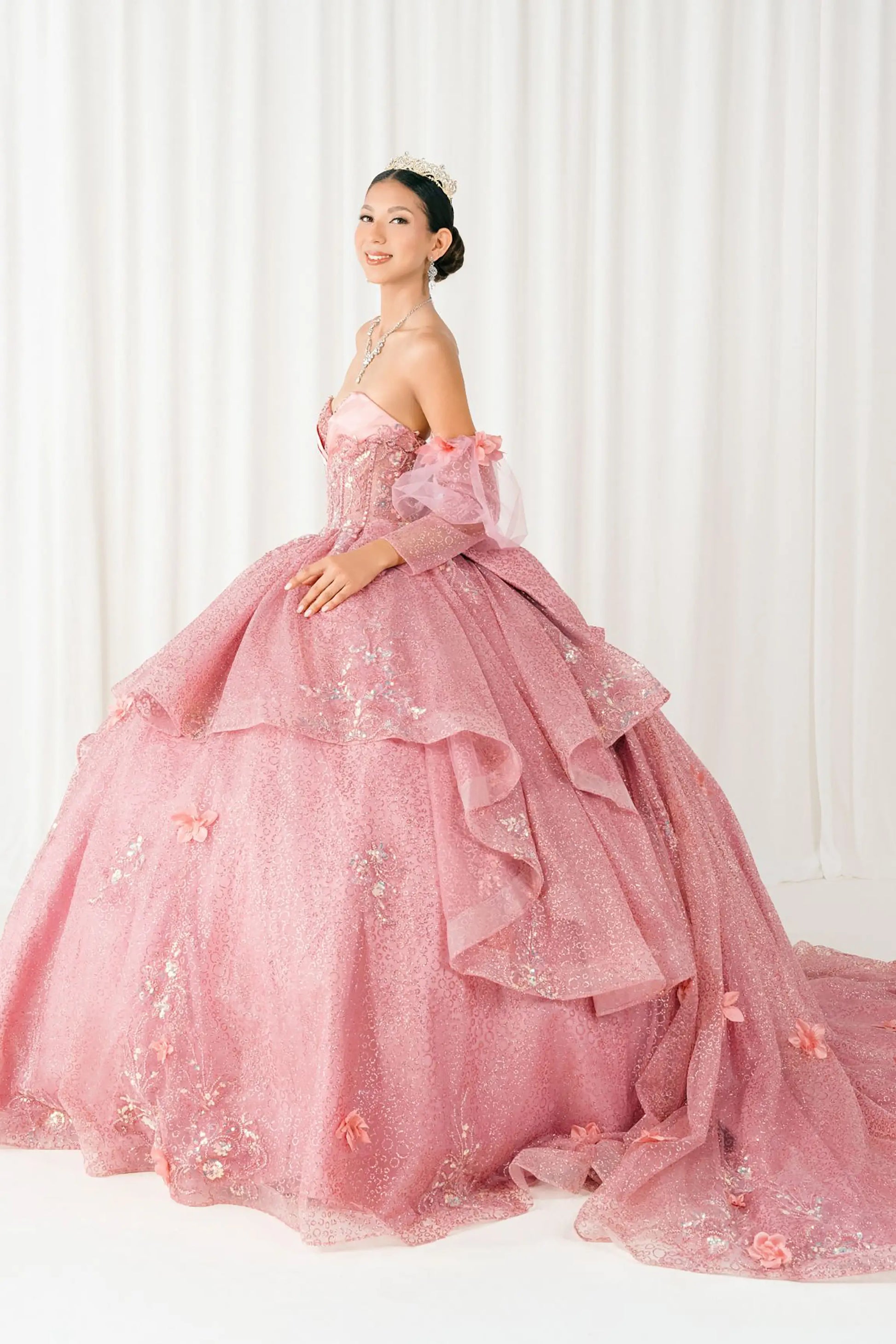 Side full-length view of Dusty Rose quinceañera ball gown with off shoulder tulle sleeves, sweetheart sequin bodice, layered glitter tulle skirt, and cathedral train