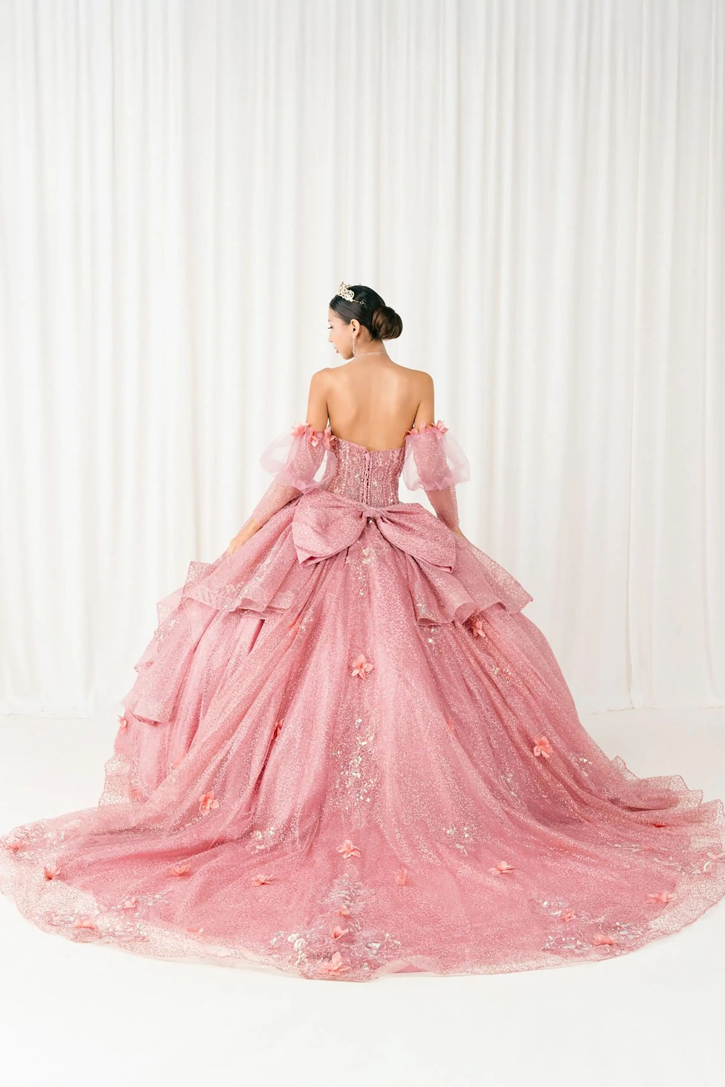 Back full-length view of Dusty Rose quinceañera ball gown with off shoulder tulle sleeves, sweetheart sequin bodice, layered glitter tulle skirt, and cathedral train