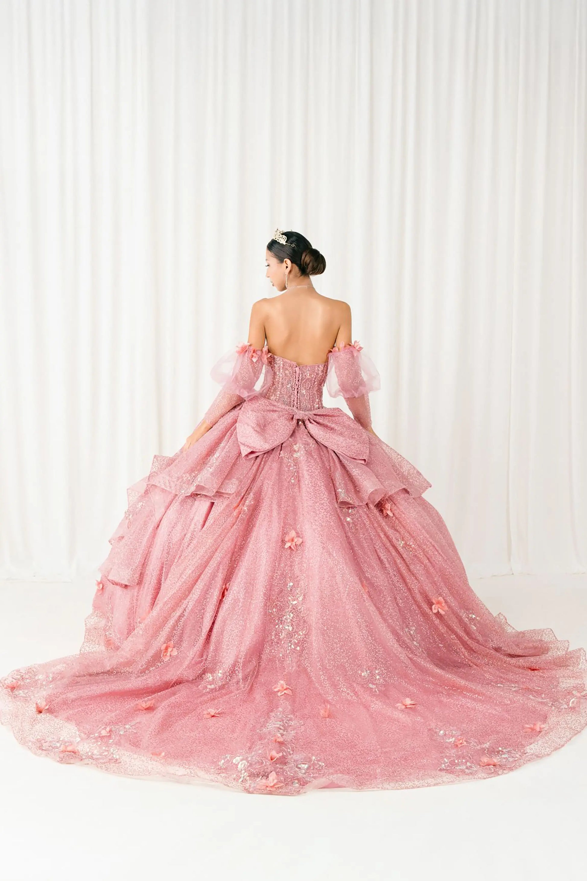 Back full-length view of Dusty Rose quinceañera ball gown with off shoulder tulle sleeves, sweetheart sequin bodice, layered glitter tulle skirt, and cathedral train