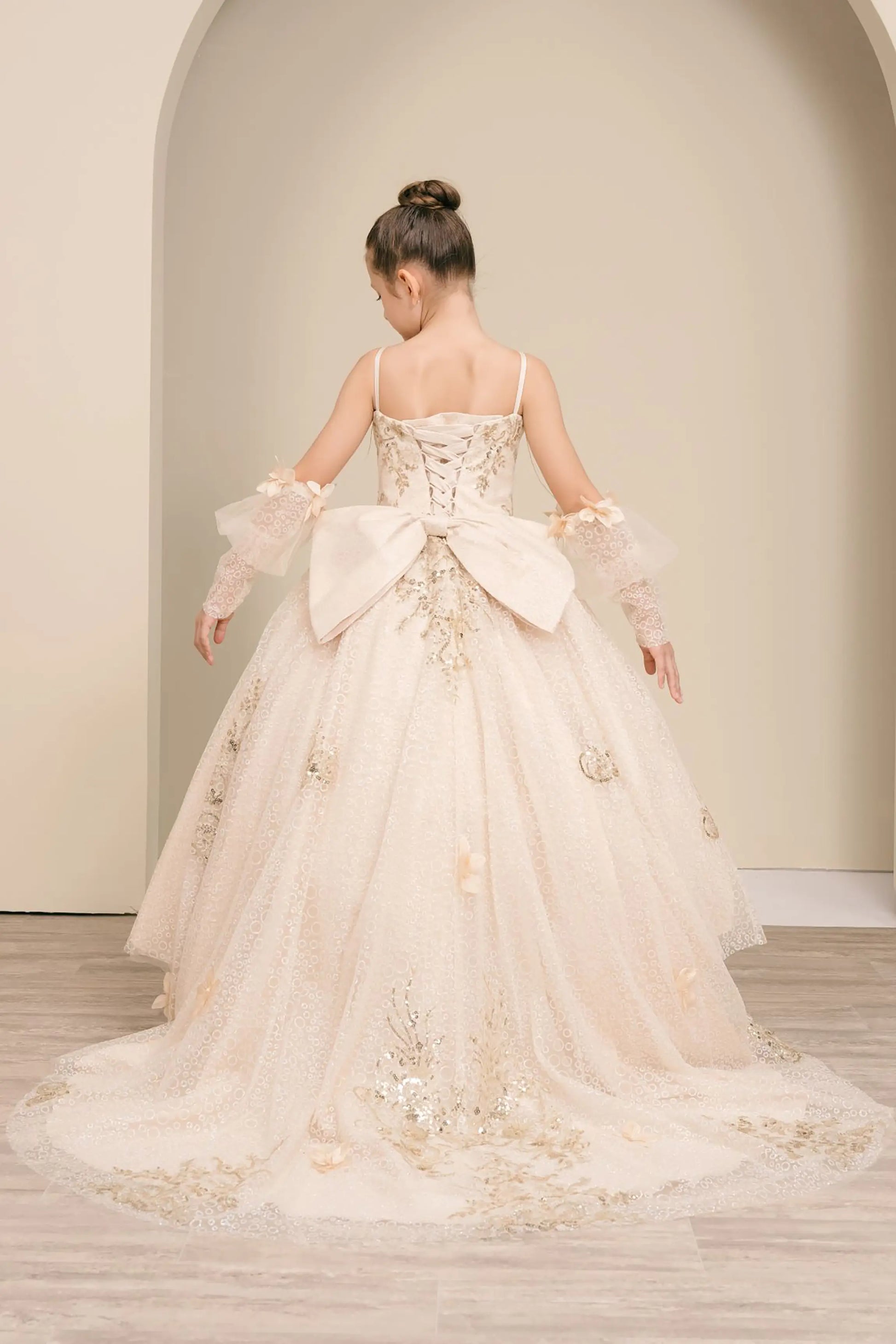 Back full-length view of Champagne mini quince ball gown with glitter floral embroidered bodice, full skirt, lace up back, oversized bow, and sheer lace gloves
