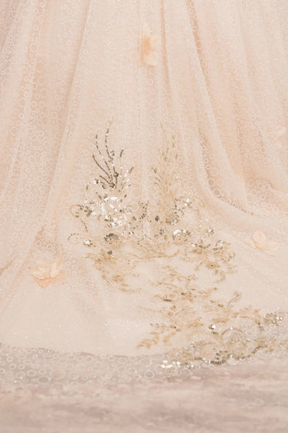 Close up view of Champagne mini quince ball gown with glitter floral embroidered bodice, full skirt, lace up back, oversized bow, and sheer lace gloves