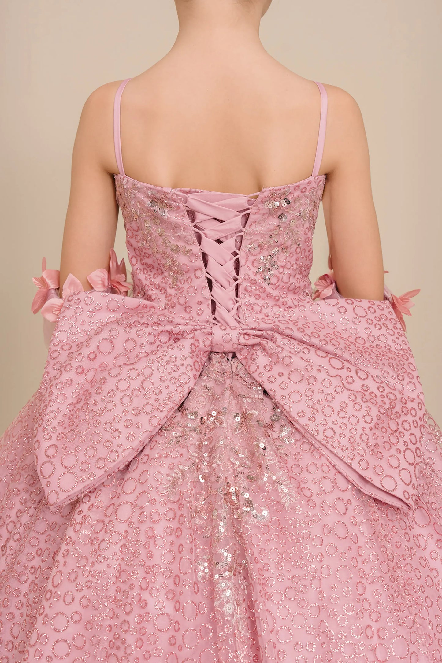 Back close up view of Dusty Rose mini quince ball gown with glitter floral embroidered bodice, full skirt, lace up back, oversized bow, and sheer lace gloves