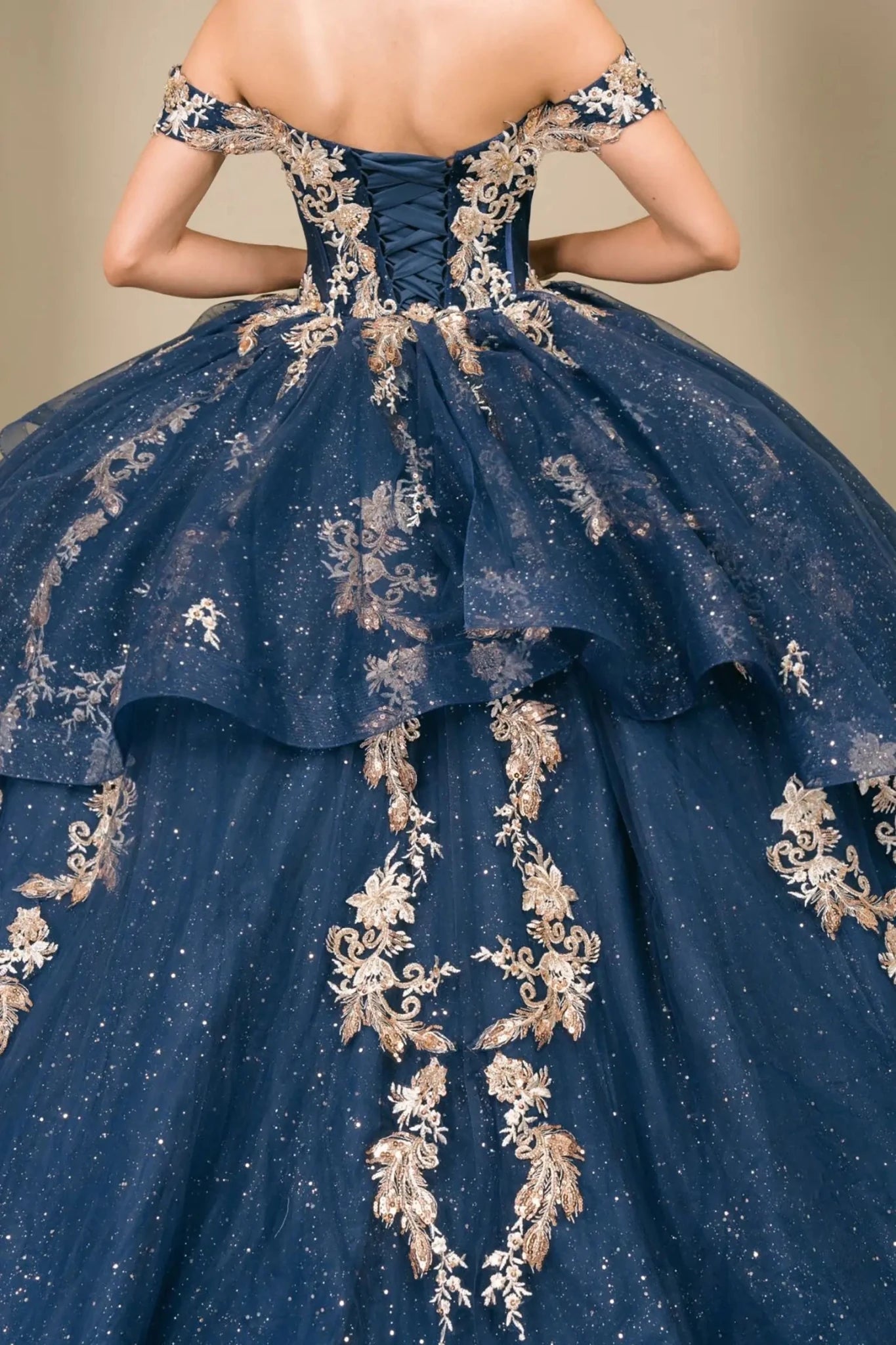 Close-up of woman back-facing in navy quinceañera dress with lace-up corset bodice, gold embroidery, detachable cape layer, and extended train detail