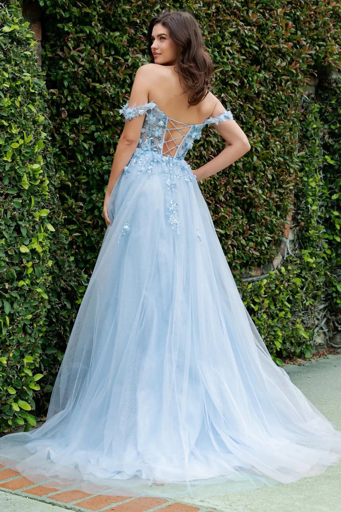 A full back view of a woman wearing a blue fairytale prom dress featuring a lace-up corset and layered tulle skirt.