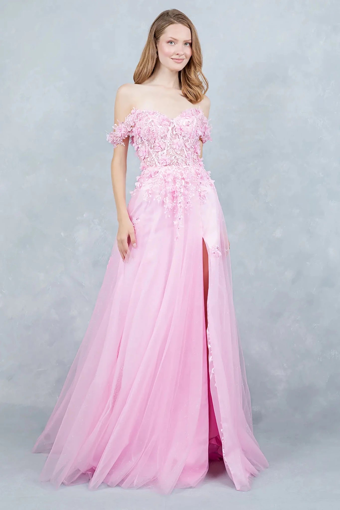 Full front view of a women wearing pink off-shoulder prom dress with floral appliqués and tulle skirt.