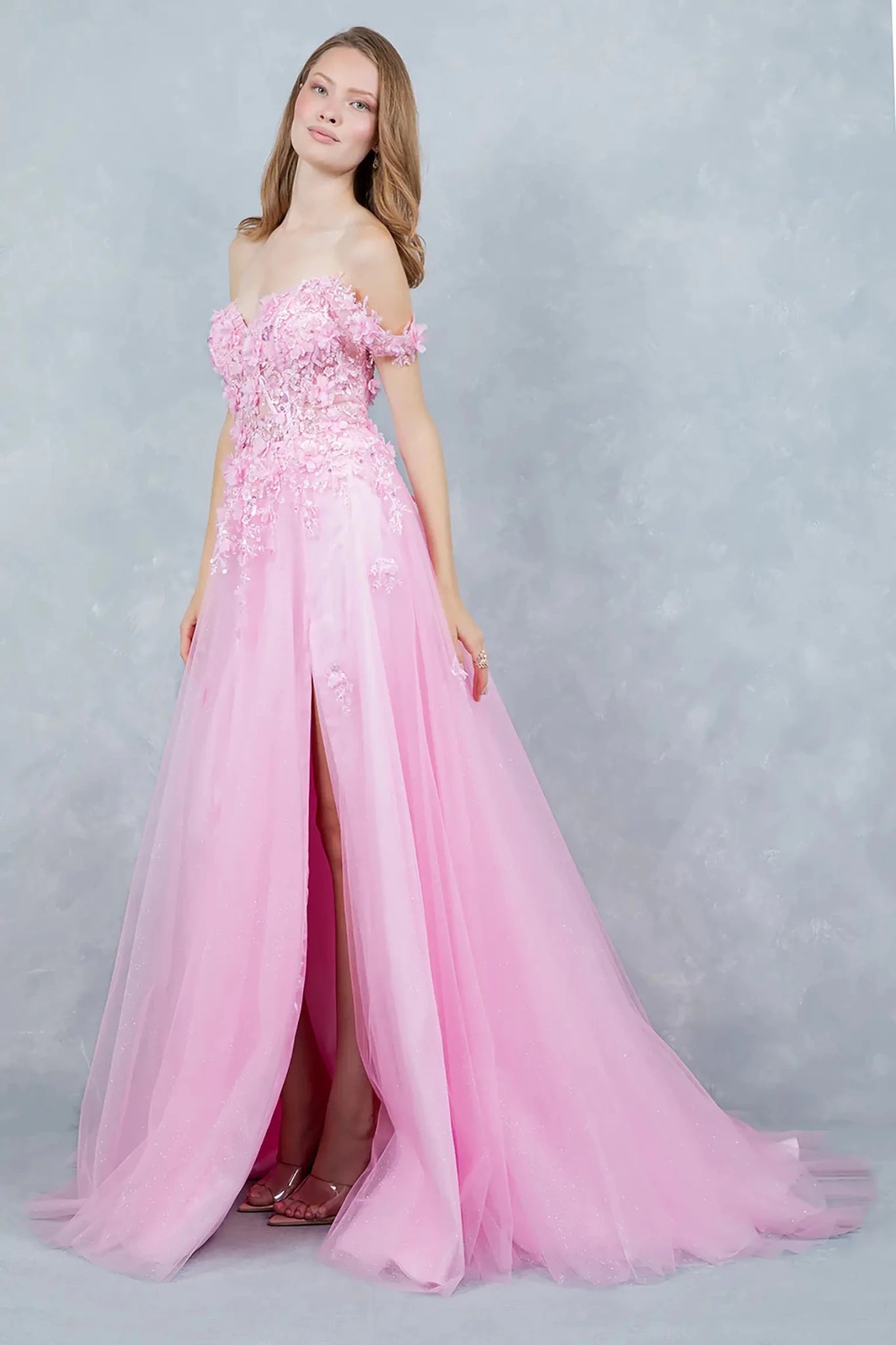 A side profile view of a woman wearing a pink prom dress, showcasing the full tulle skirt and graceful silhouette.