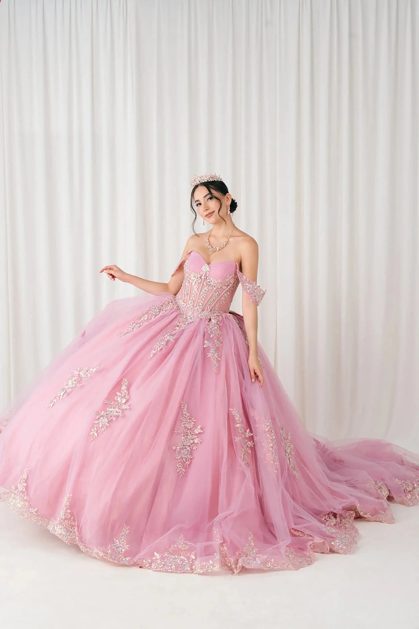 Front full-length view of Dusty Rose Off shoulder quinceañera ball gown with beaded corset, floral appliqués, layered tulle skirt, cathedral length train, and bow