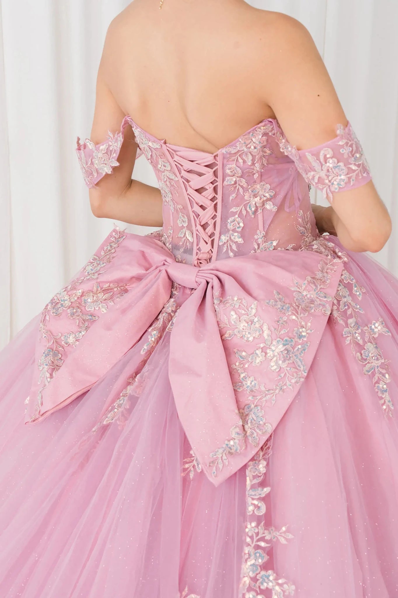 Back close-up view of Dusty Rose Off shoulder quinceañera ball gown with beaded corset, floral appliqués, layered tulle skirt, cathedral length train, and bow