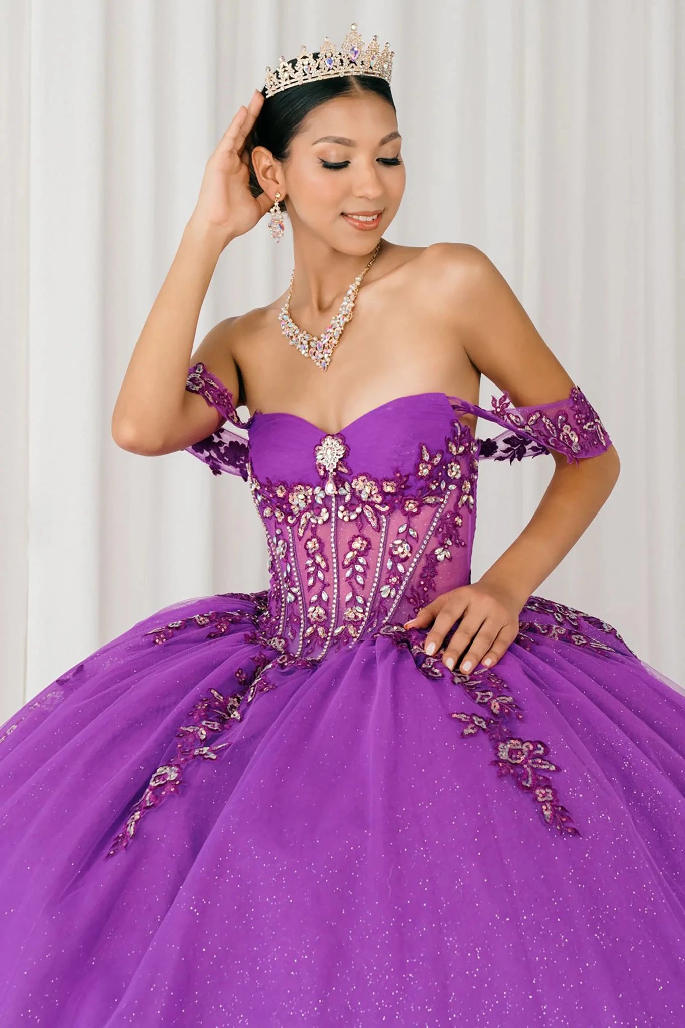 Front close-up view of Magenta Off shoulder quinceañera ball gown with beaded corset, floral appliqués, layered tulle skirt, cathedral length train, and bow