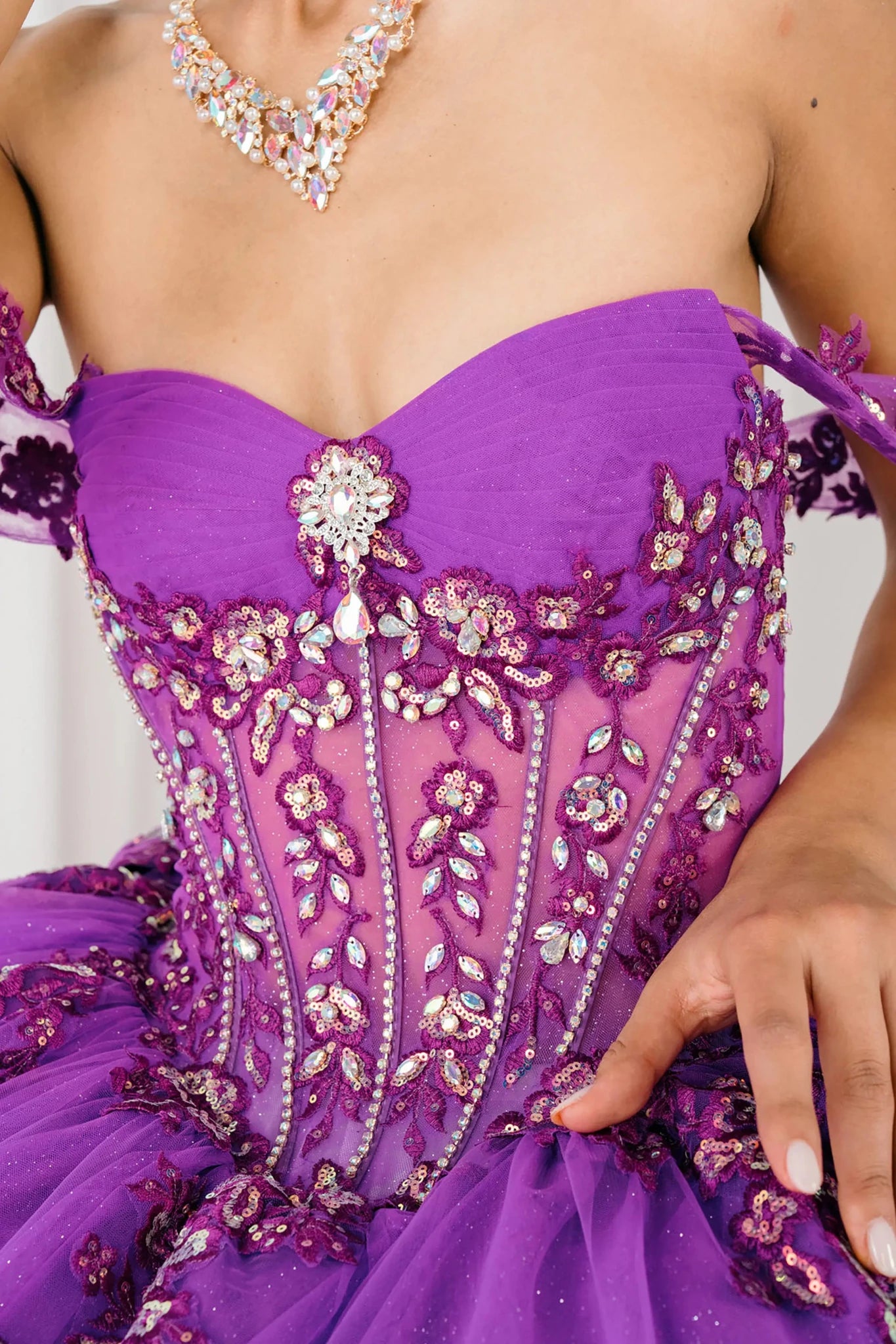 Front close-up view of Magenta Off shoulder quinceañera ball gown with beaded corset, floral appliqués, layered tulle skirt, cathedral length train, and bow