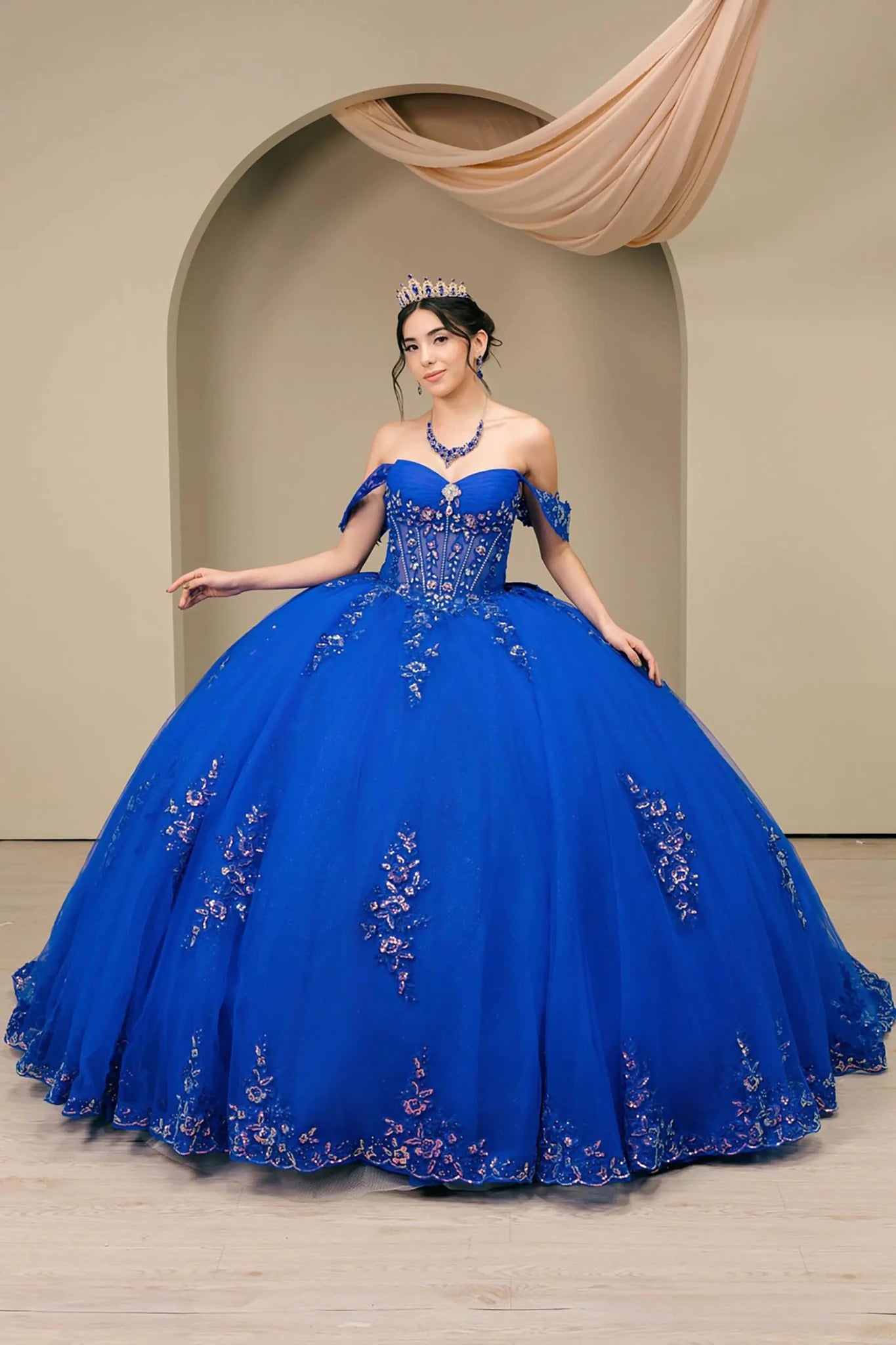Front full-length view of Royal Off shoulder quinceañera ball gown with beaded corset, floral appliqués, layered tulle skirt, cathedral length train, and bow