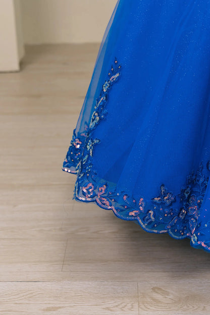 Close up view Royal mini quince off shoulder ball gown with embroidered bodice, gemstone accent, glitter tulle skirt, lace up back, and oversized bow.