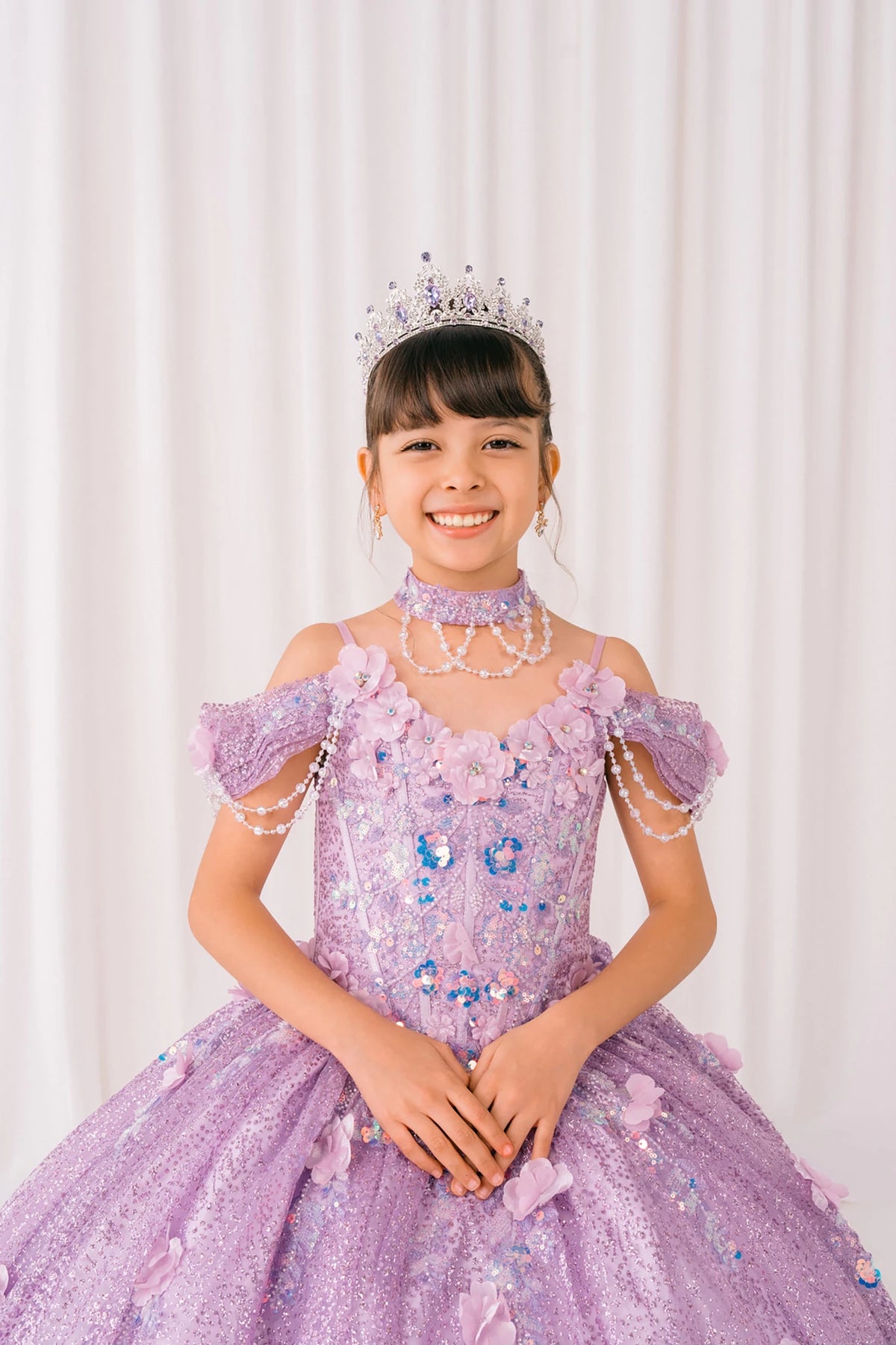 Lilac front view kids mini quinceañera mini quince dress with off-shoulder 3D floral applique, pearls and glitter tulle skirt.