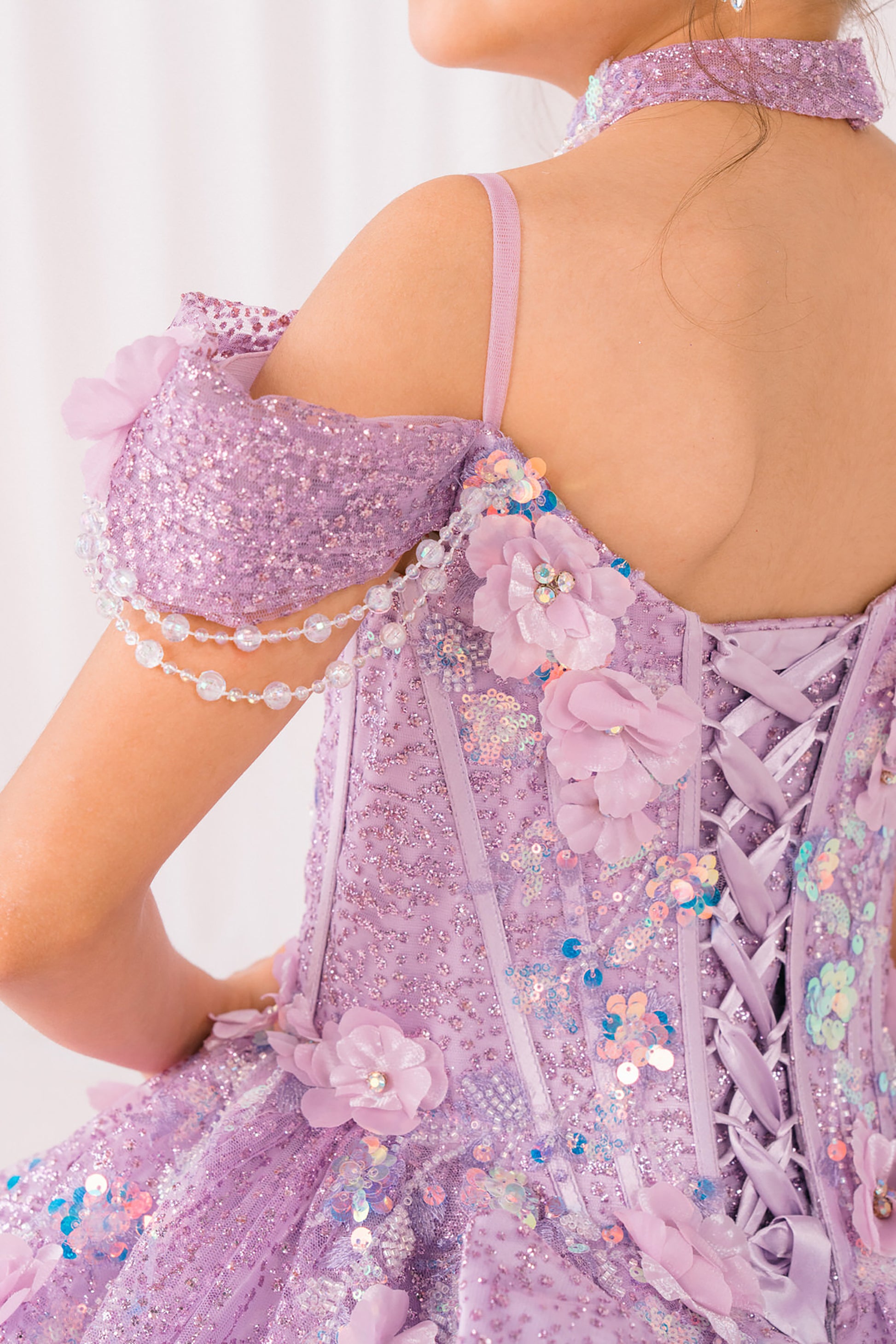 Close-up of a person wearing a sparkling lilac mini quince dress with floral details on a white background