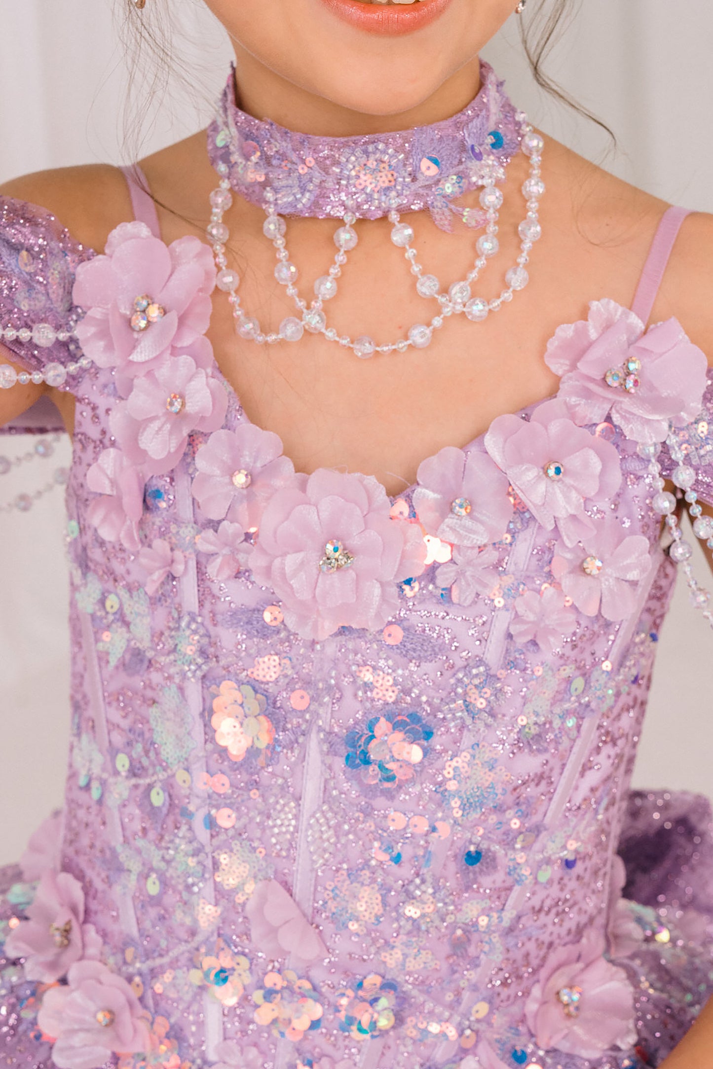 Close-up of a person wearing a sparkling lilac mini quince dress with floral details and jewelry.