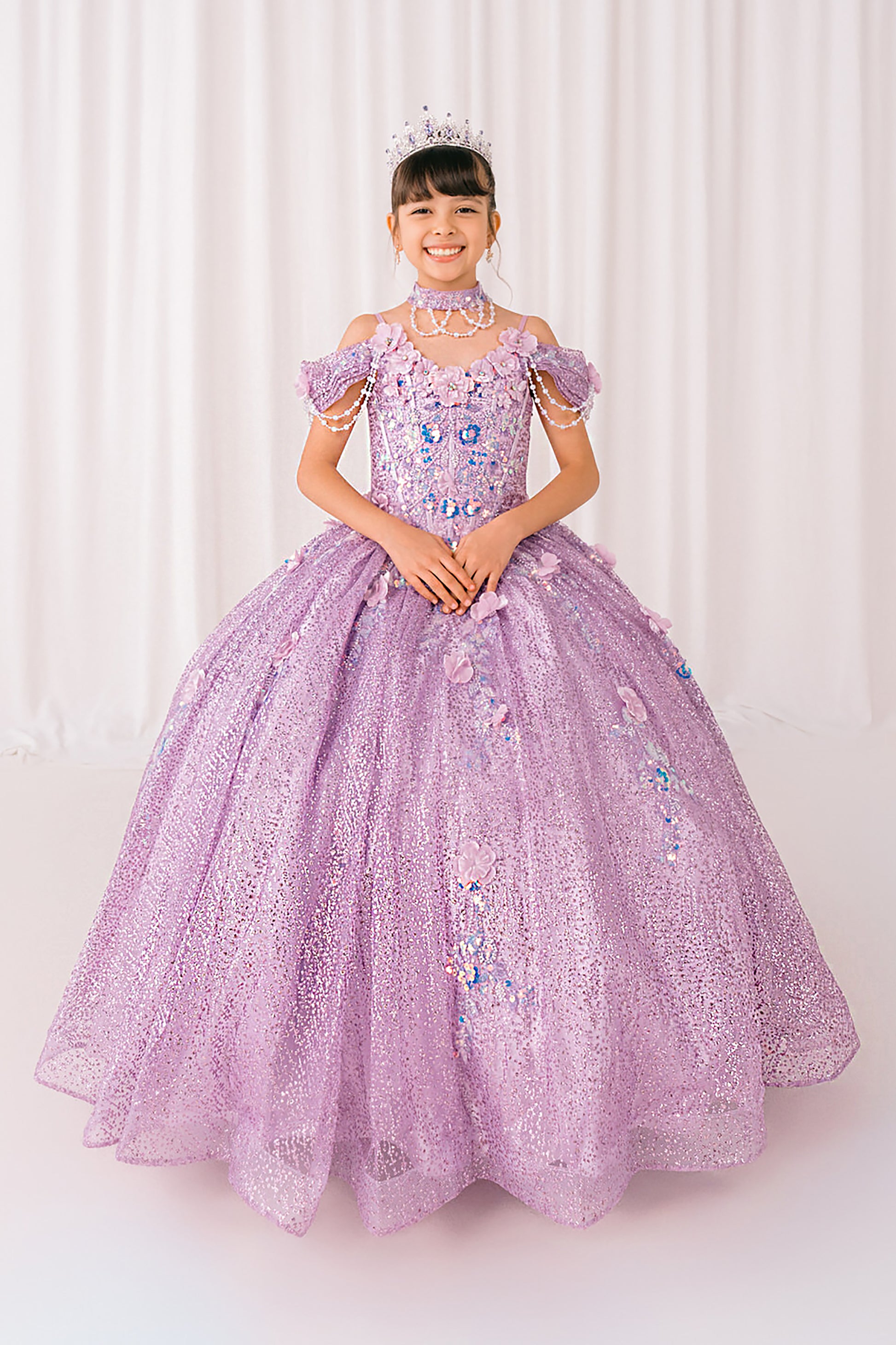 Young girl in a lilac mini quince dress with floral embellishments against a white curtain background
