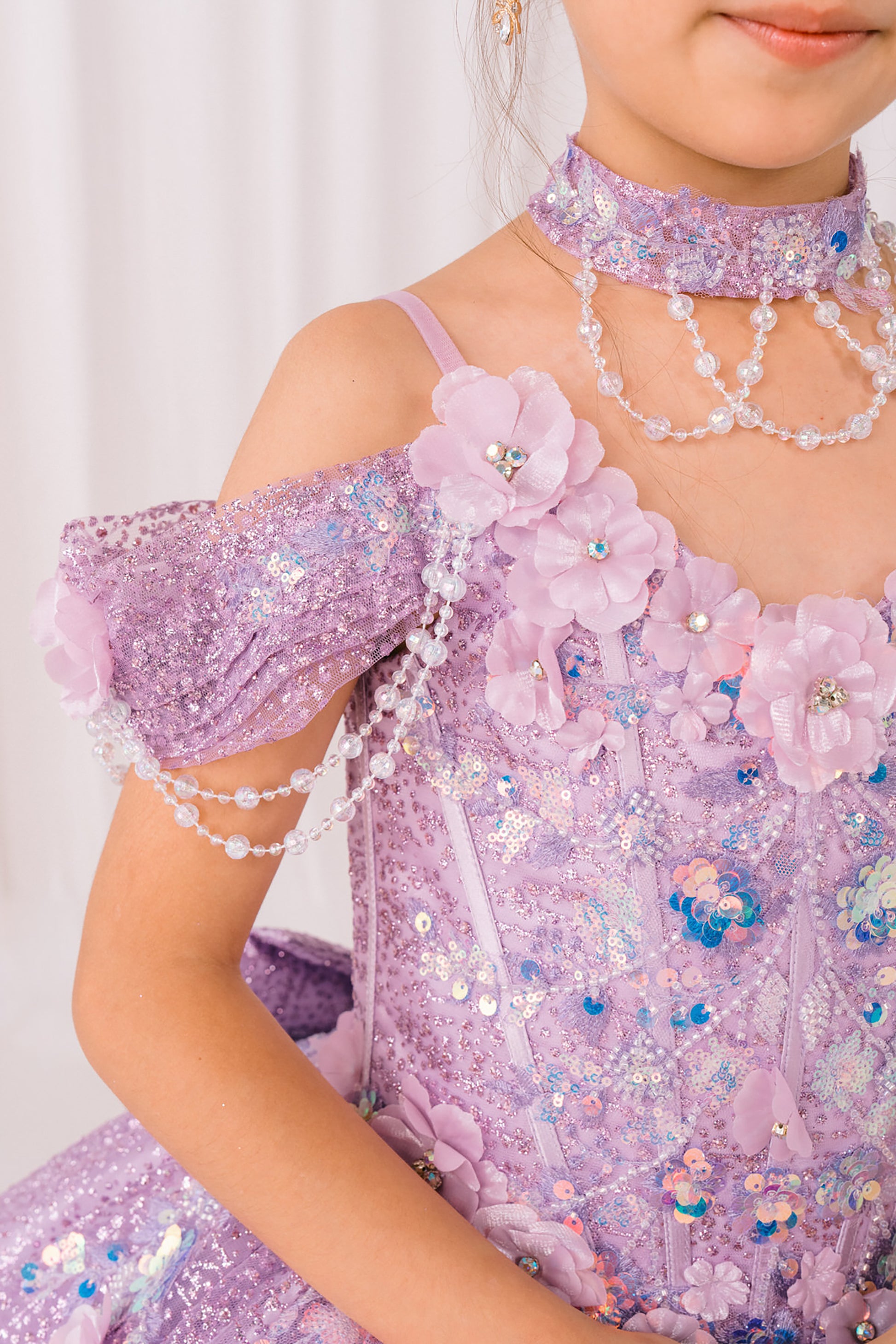 Child wearing a sparkling lilac mini quince dress with floral details and jewelry against a white background