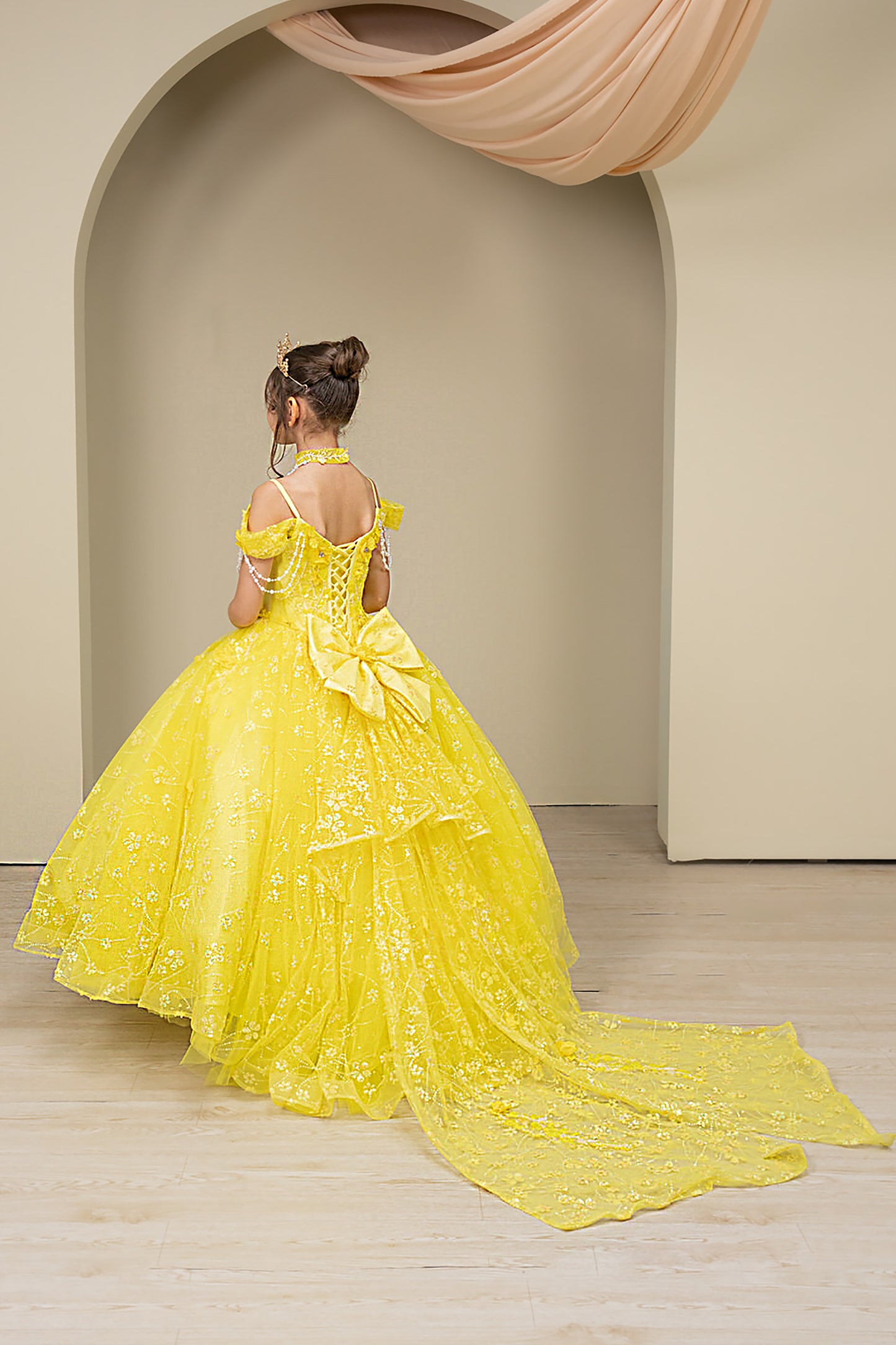 kid in a yellow mini quince ball gown standing in an archway with beige walls.