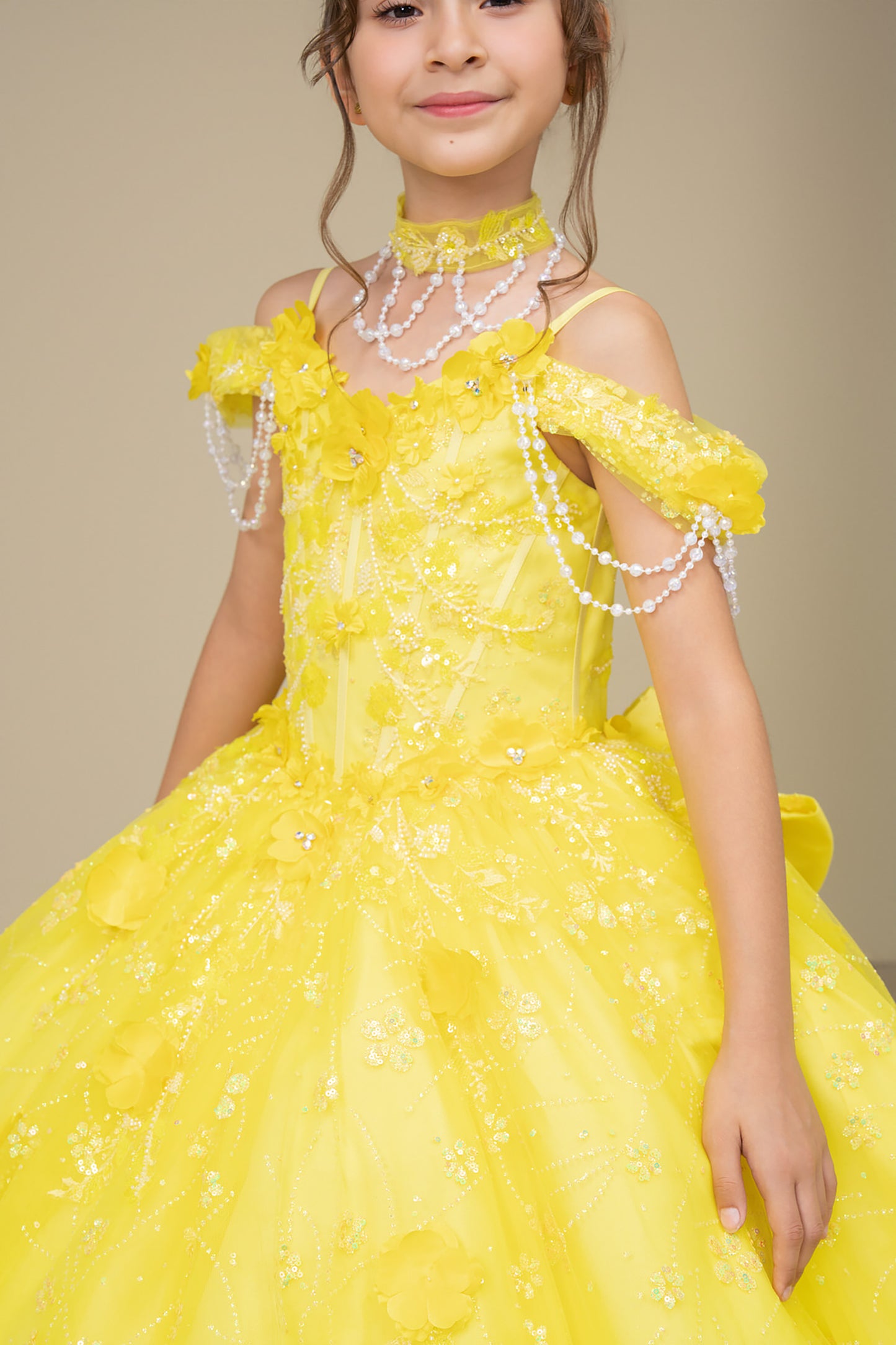 Young girl in a yellow dress with floral details and pearl accessories against a beige background