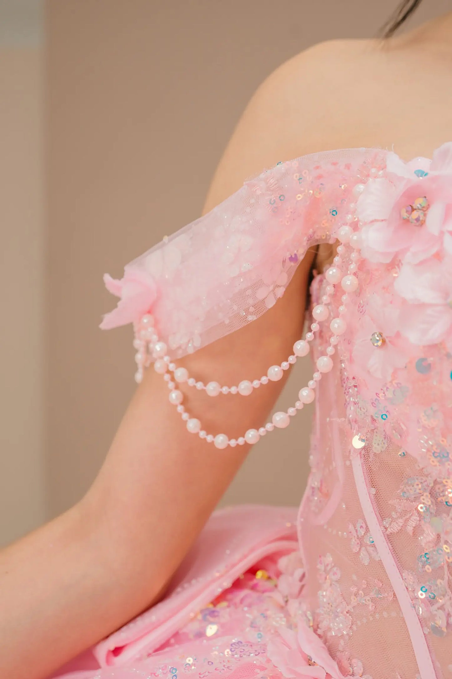 Side close-up view of a woman wearing pink quinceañera dress highlighting layered glitter tulle, sweetheart neckline, and embellished bodice.
