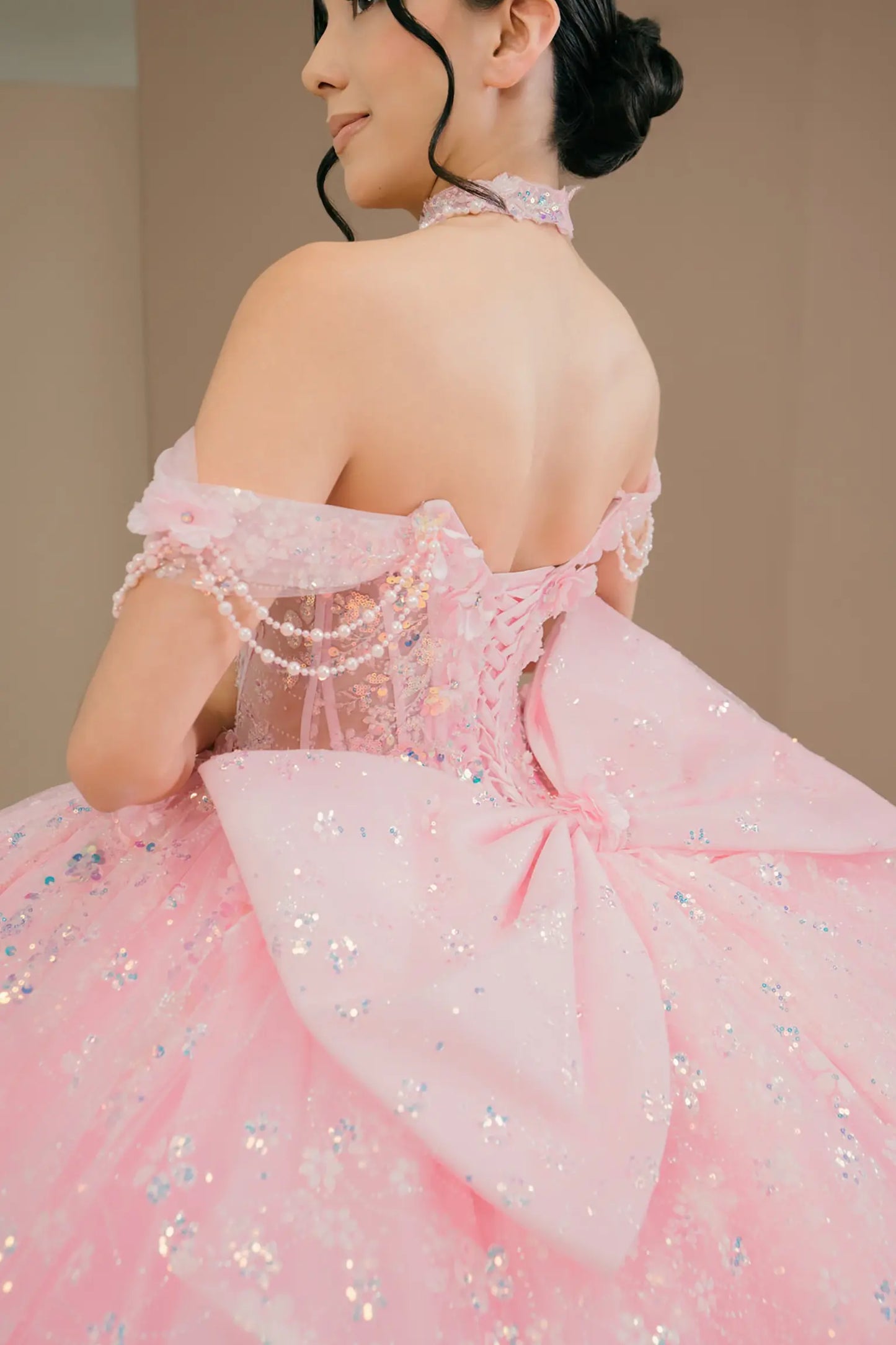 Bodice back close-up of a woman wearing pink quinceañera dress with beadwork detail, sequins, and lace-up corset design.