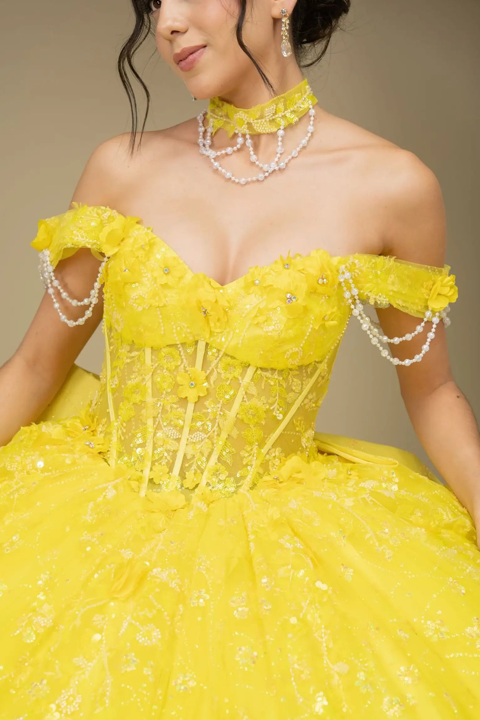 Bodice close-up of a woman wearing yellow quinceañera dress showing floral appliques, sequins, and intricate beadwork details.