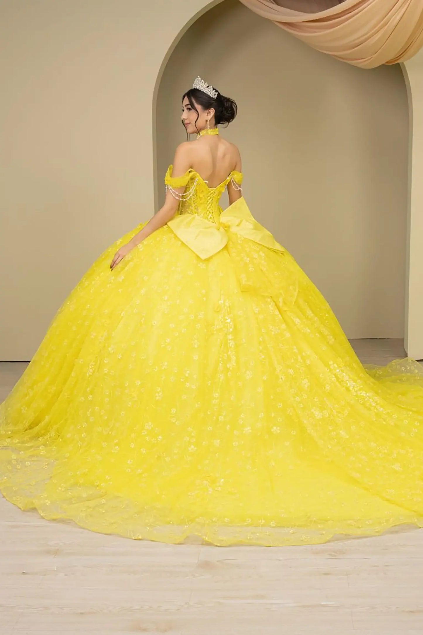 Back view of a woman wearing yellow quinceañera dress with voluminous glitter tulle skirt, lace-up corset closure, and floral applique accents.