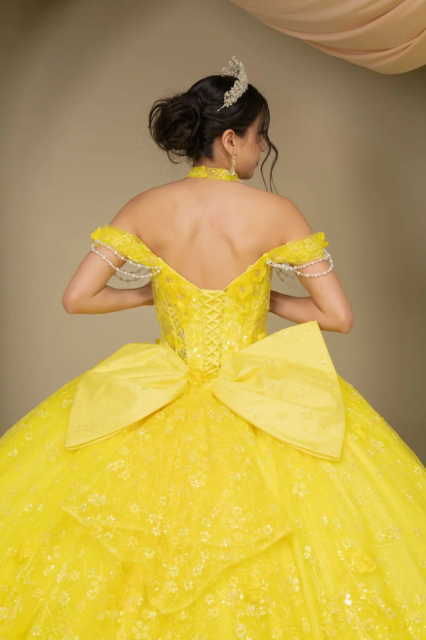 Back close-up view of a woman wearing yellow quinceañera dress highlighting layered glitter tulle, sweetheart neckline, and embellished bodice.