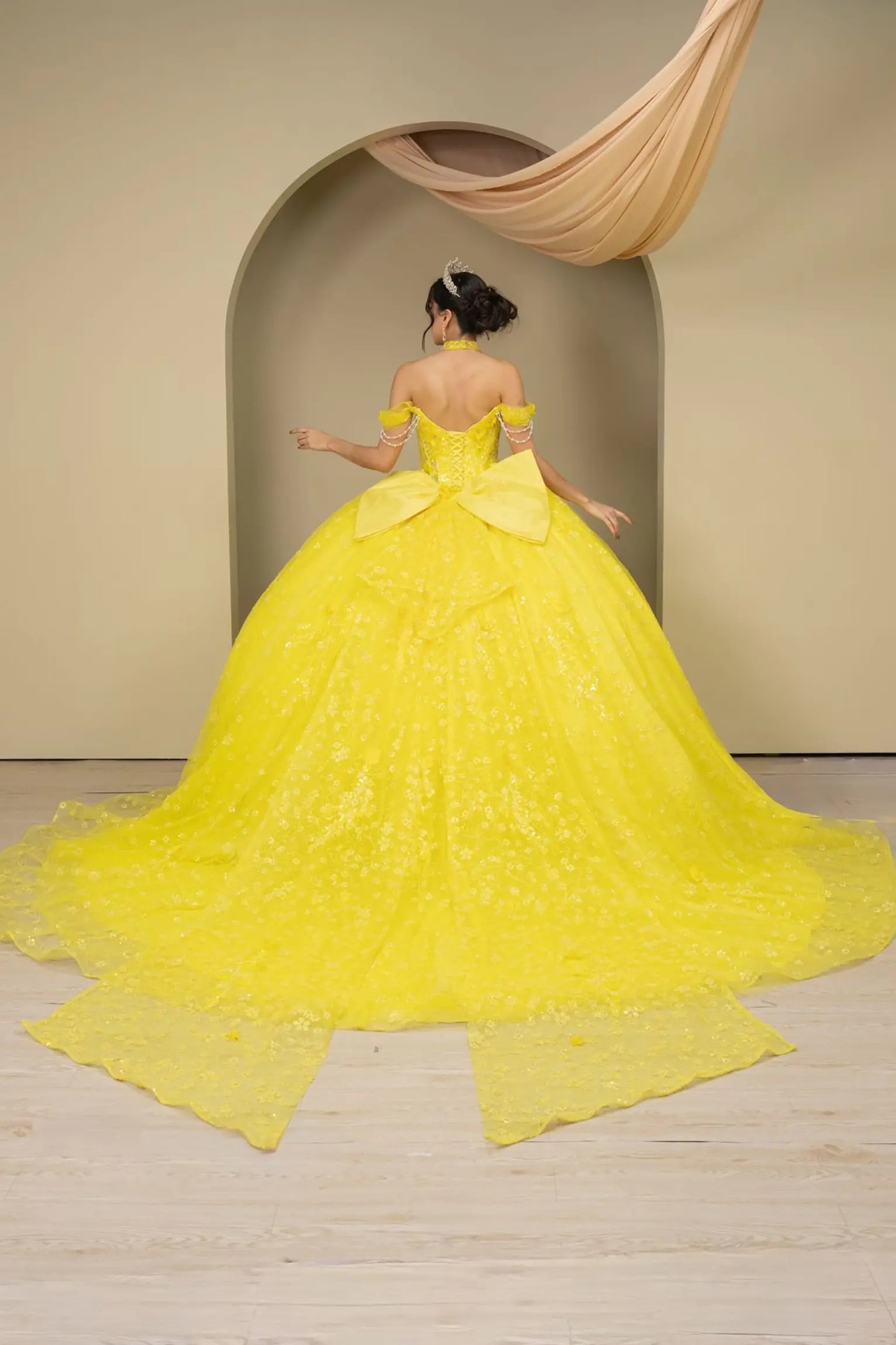 Full back view of a woman wearing yellow quinceañera dress with glitter tulle skirt, off-shoulder sweetheart neckline, and beaded corset bodice.