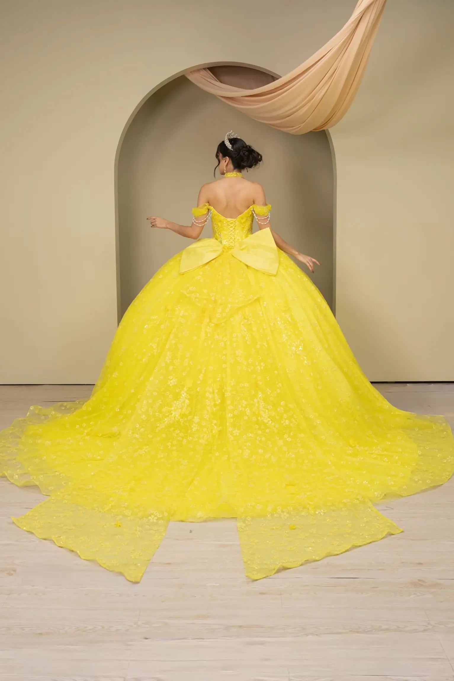 Full back view of a woman wearing yellow quinceañera dress with glitter tulle skirt, off-shoulder sweetheart neckline, and beaded corset bodice.