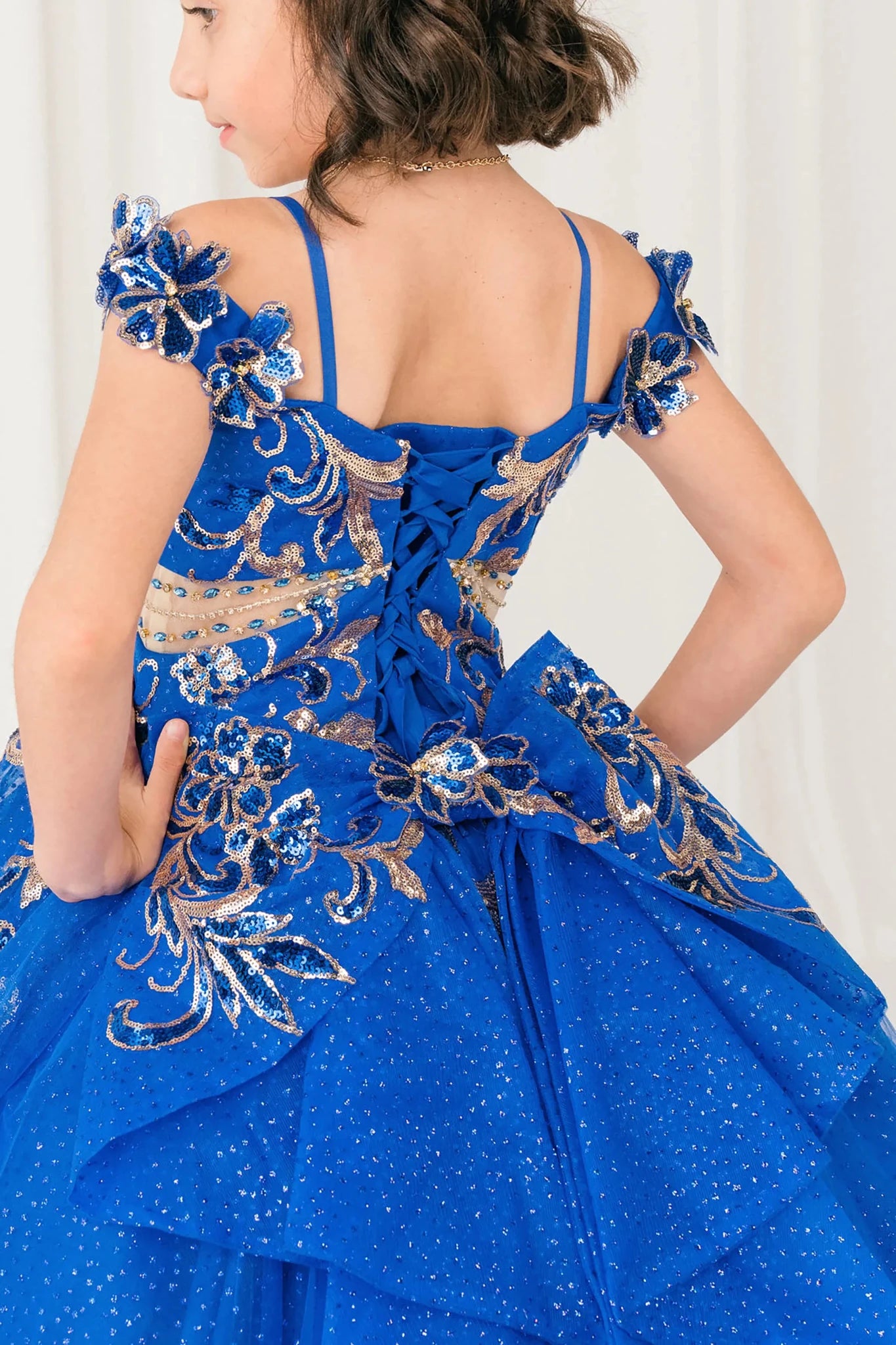 Back close up view of Royal mini quince mini quince dress with off shoulder floral embroidered bodice, glitter tulle skirt, lace up back, and layered bow.