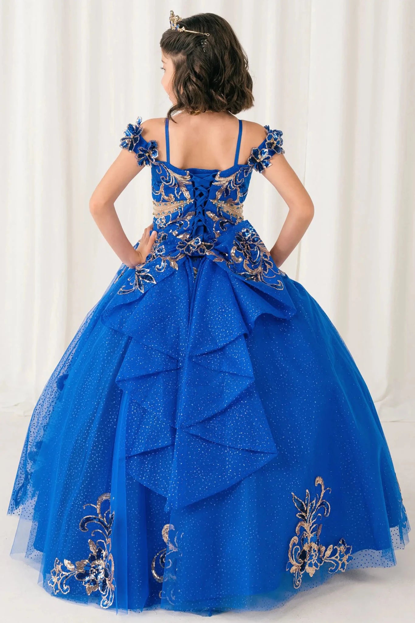 Back full-length view of Royal mini quince mini quince dress with off shoulder floral embroidered bodice, glitter tulle skirt, lace up back, and layered bow.