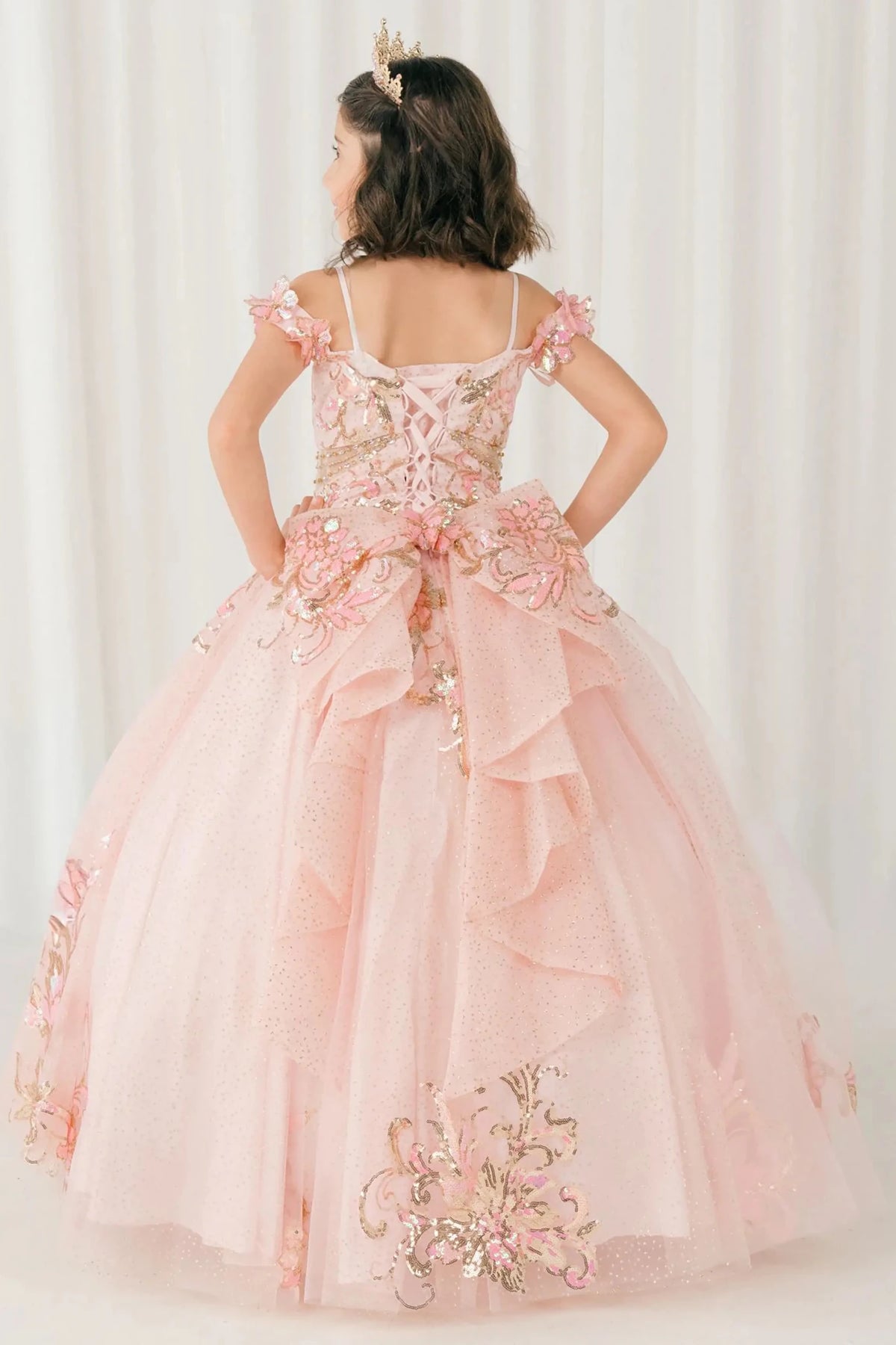 Side full-length view of Pink mini quince mini quince dress with off shoulder floral embroidered bodice, glitter tulle skirt, lace up back, and layered bow.