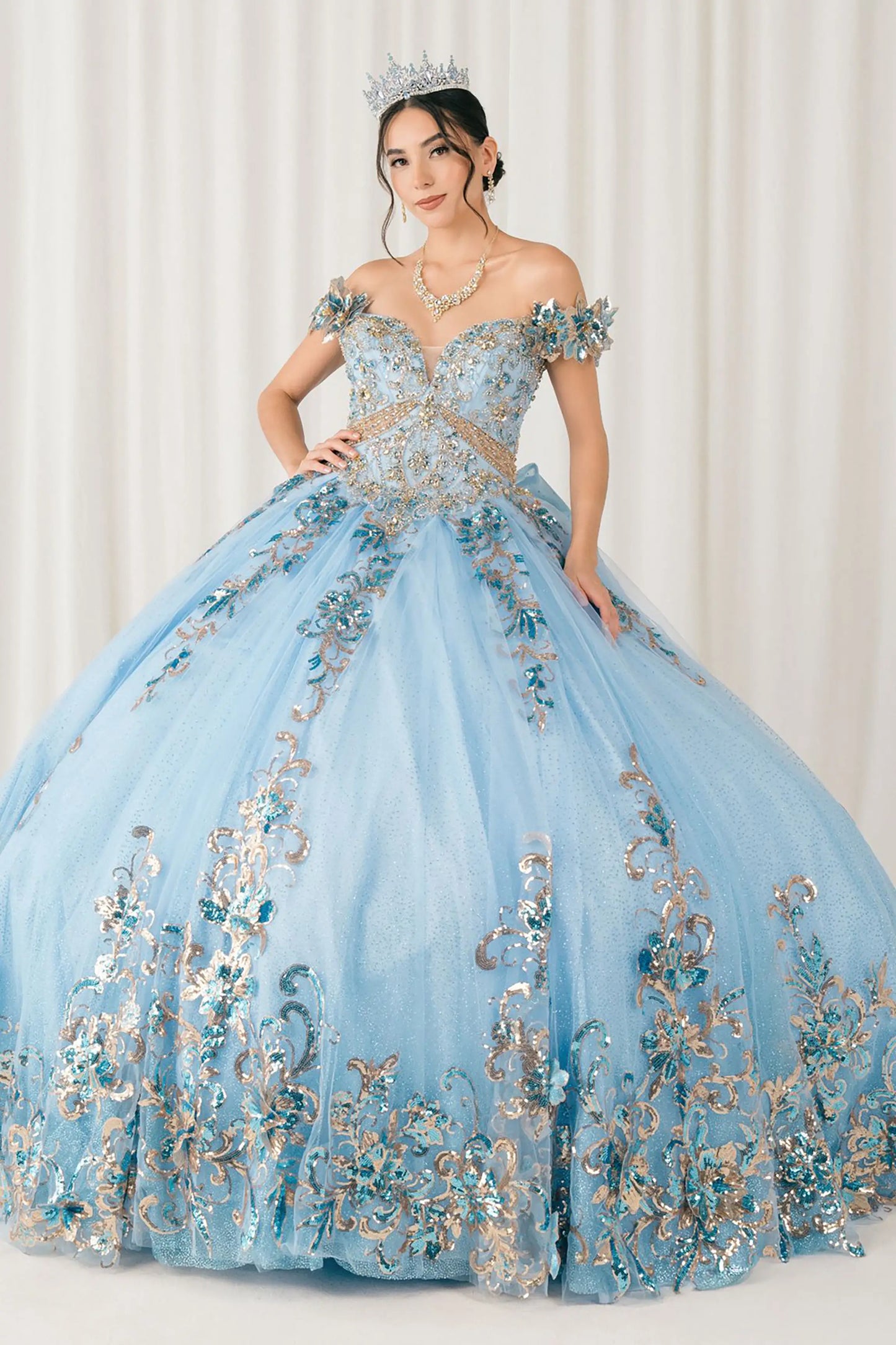 Front full-length view of Blue quinceañera ball gown with off shoulder bodice, gold embroidery, floral appliqués, voluminous tulle skirt, corset back, and oversized bow