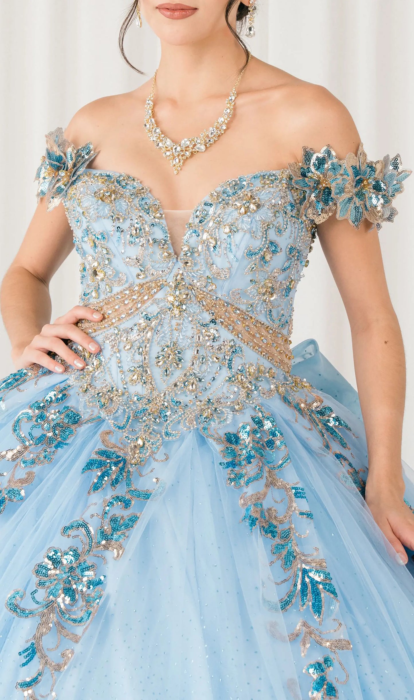 Front close-up Blue quinceañera ball gown with off shoulder bodice, gold embroidery, floral appliqués, voluminous tulle skirt, corset back, and oversized bow