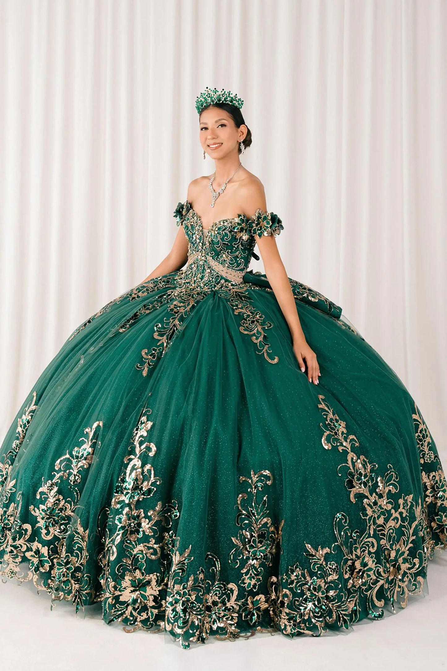 Front full-length view of Hunter Green quinceañera ball gown with off shoulder bodice, gold embroidery, floral appliqués, voluminous tulle skirt, corset back, and oversized bow
