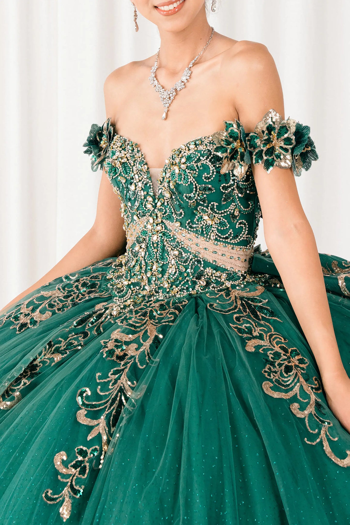 Front close-up Blue Hunter Green quinceañera ball gown with off shoulder bodice, gold embroidery, floral appliqués, voluminous tulle skirt, corset back, and oversized bow