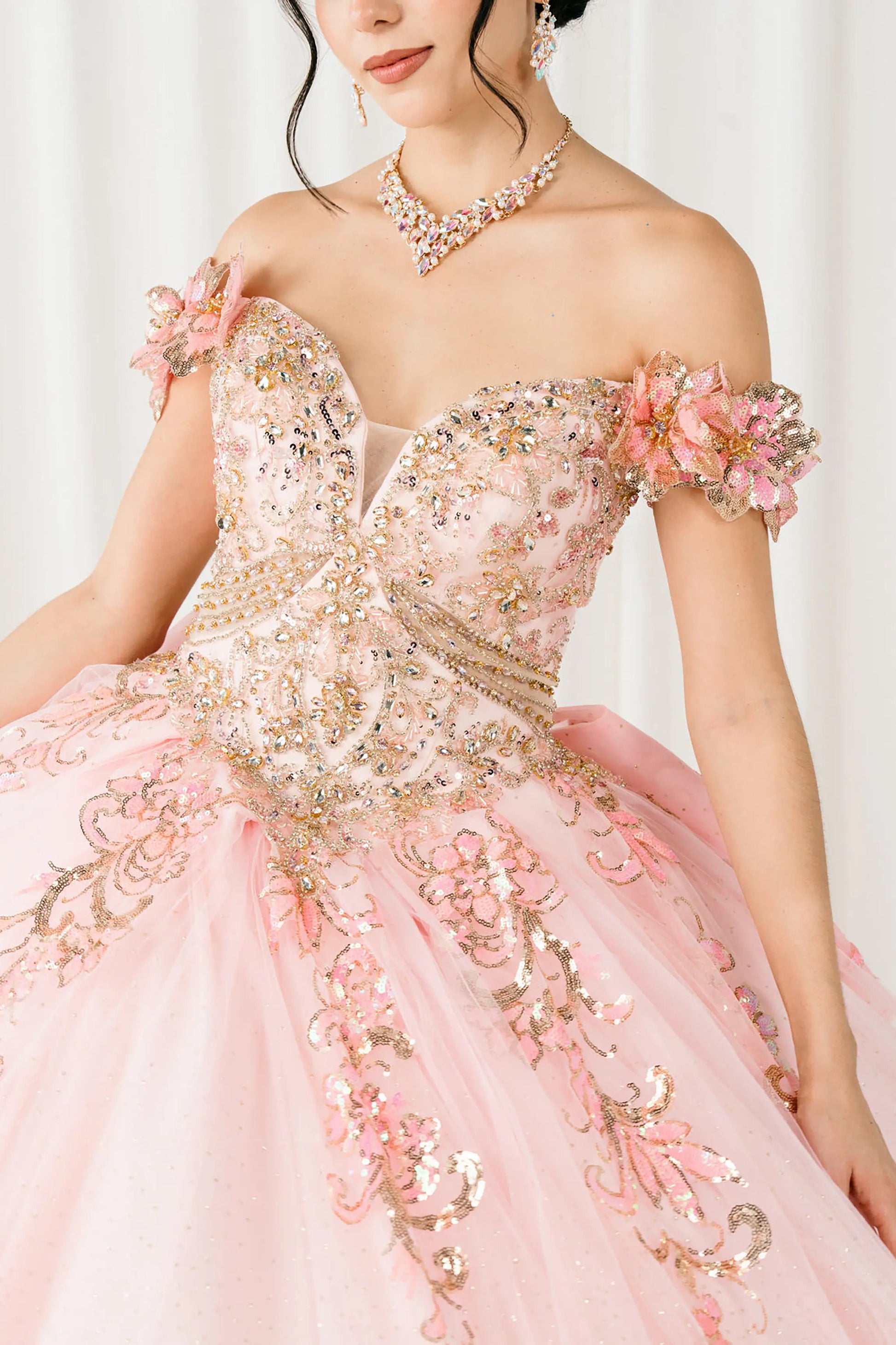 Front close-up full-length view of Pink quinceañera ball gown with off shoulder bodice, gold embroidery, floral appliqués, voluminous tulle skirt, corset back, and oversized bow