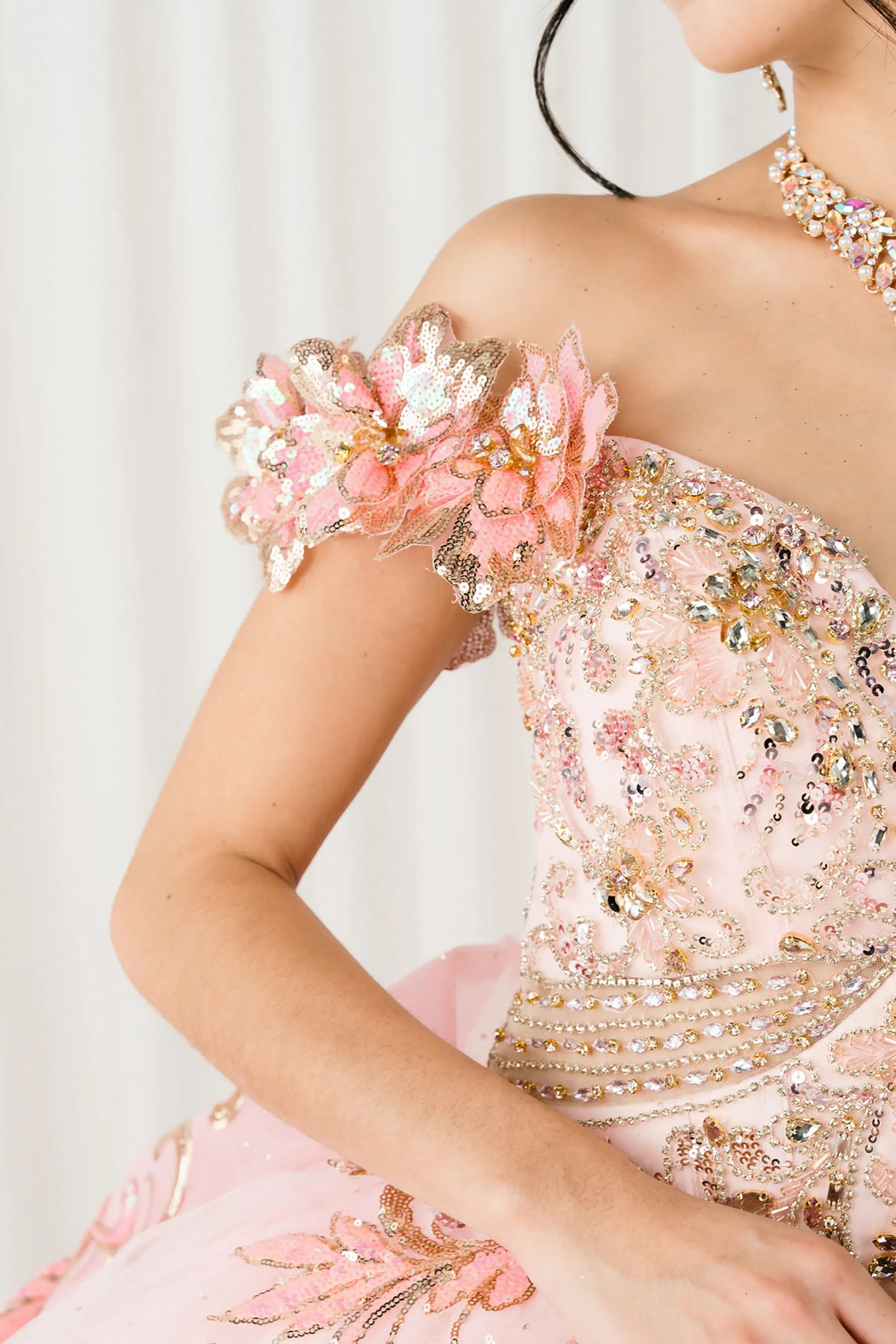 Side half close-up view of Pink quinceañera ball gown with off shoulder bodice, gold embroidery, floral appliqués, voluminous tulle skirt, corset back, and oversized bow