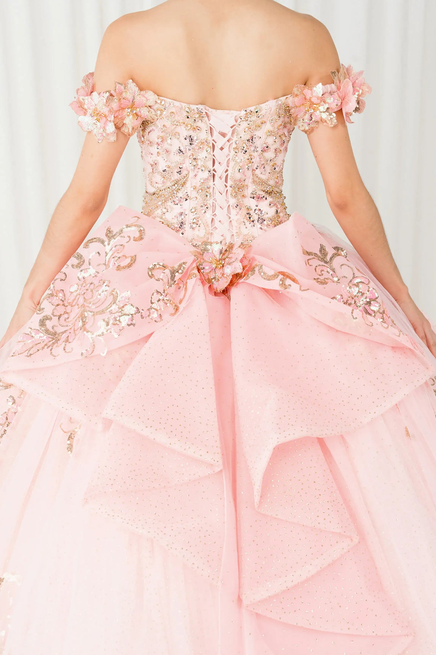 Black close-up Pink quinceañera ball gown with off shoulder bodice, gold embroidery, floral appliqués, voluminous tulle skirt, corset back, and oversized bow
