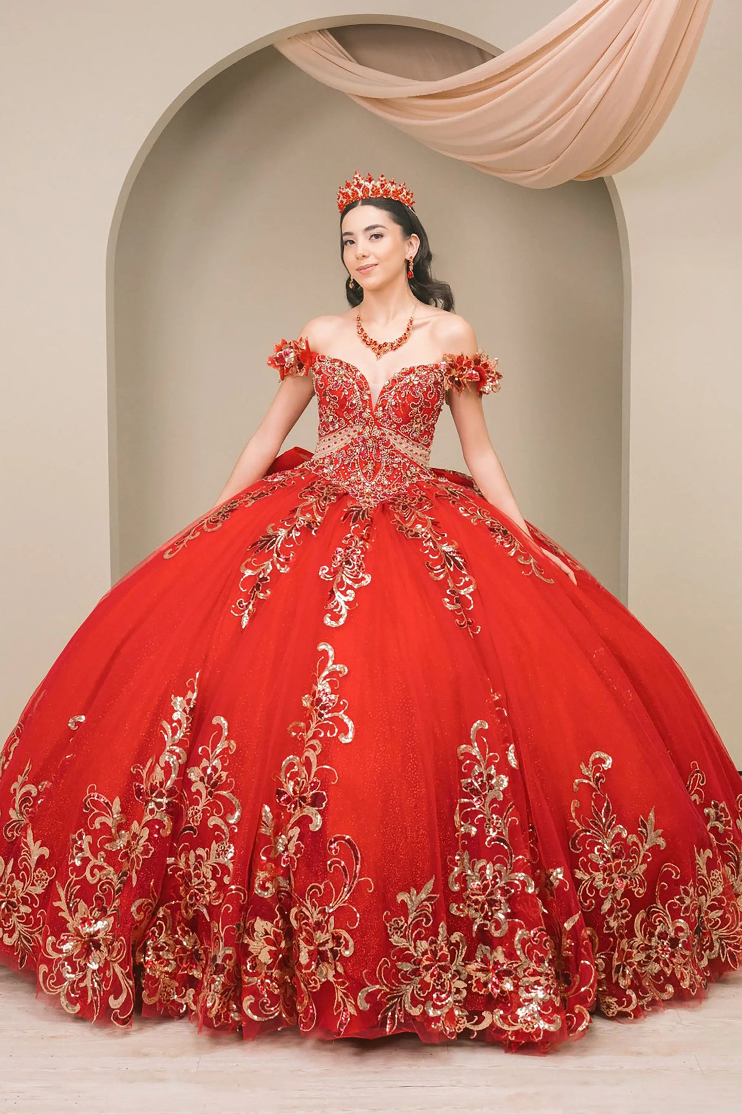 Front full-length view of Red quinceañera ball gown with off shoulder bodice, gold embroidery, floral appliqués, voluminous tulle skirt, corset back, and oversized bow