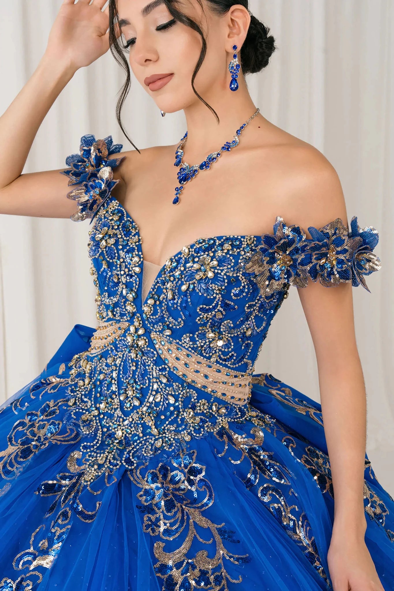 Front close-up Royal quinceañera ball gown with off shoulder bodice, gold embroidery, floral appliqués, voluminous tulle skirt, corset back, and oversized bow