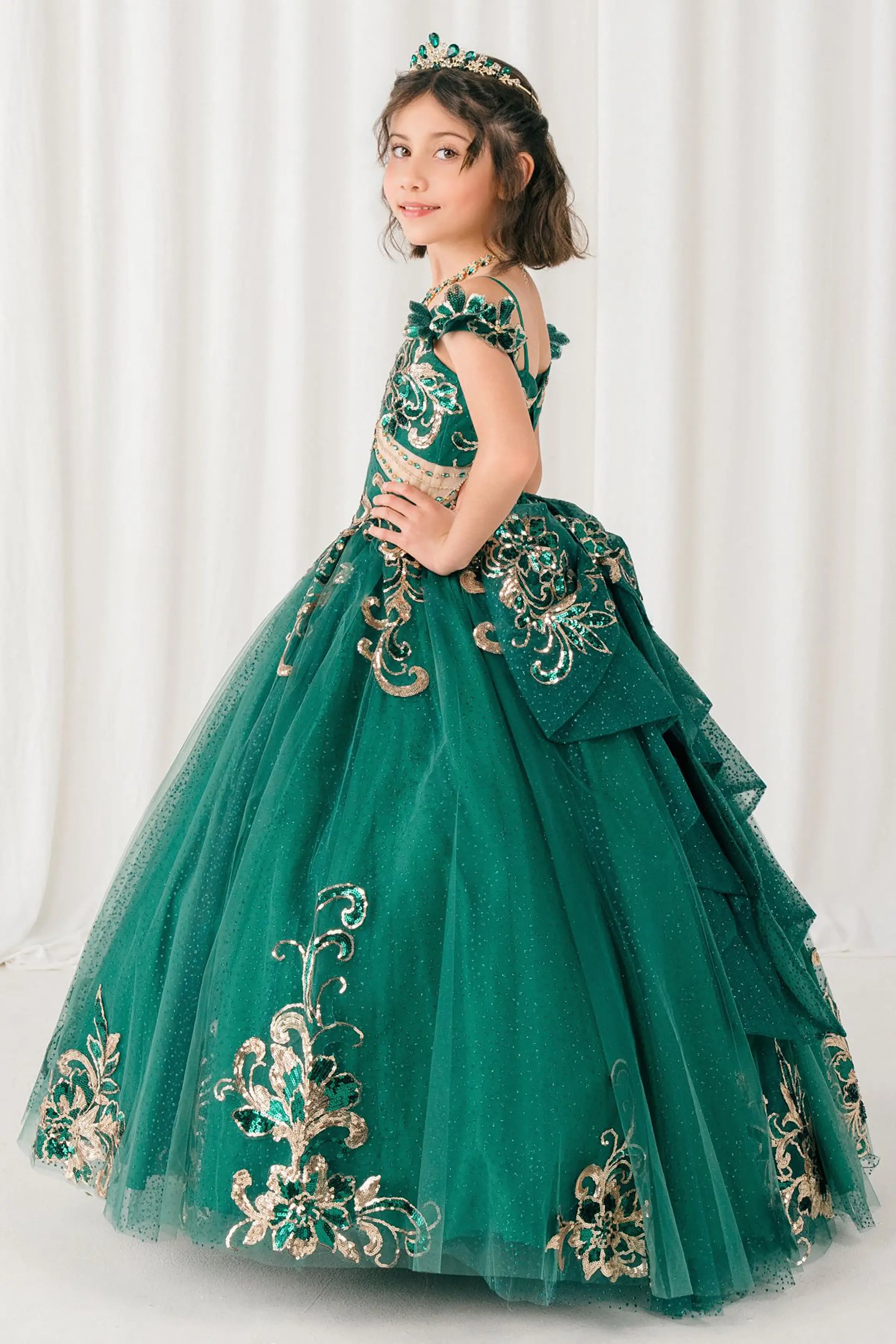 Side full-length view of Hunter green mini quince ball gown with off shoulder floral embroidered bodice, glitter tulle skirt, lace up back, and layered bow