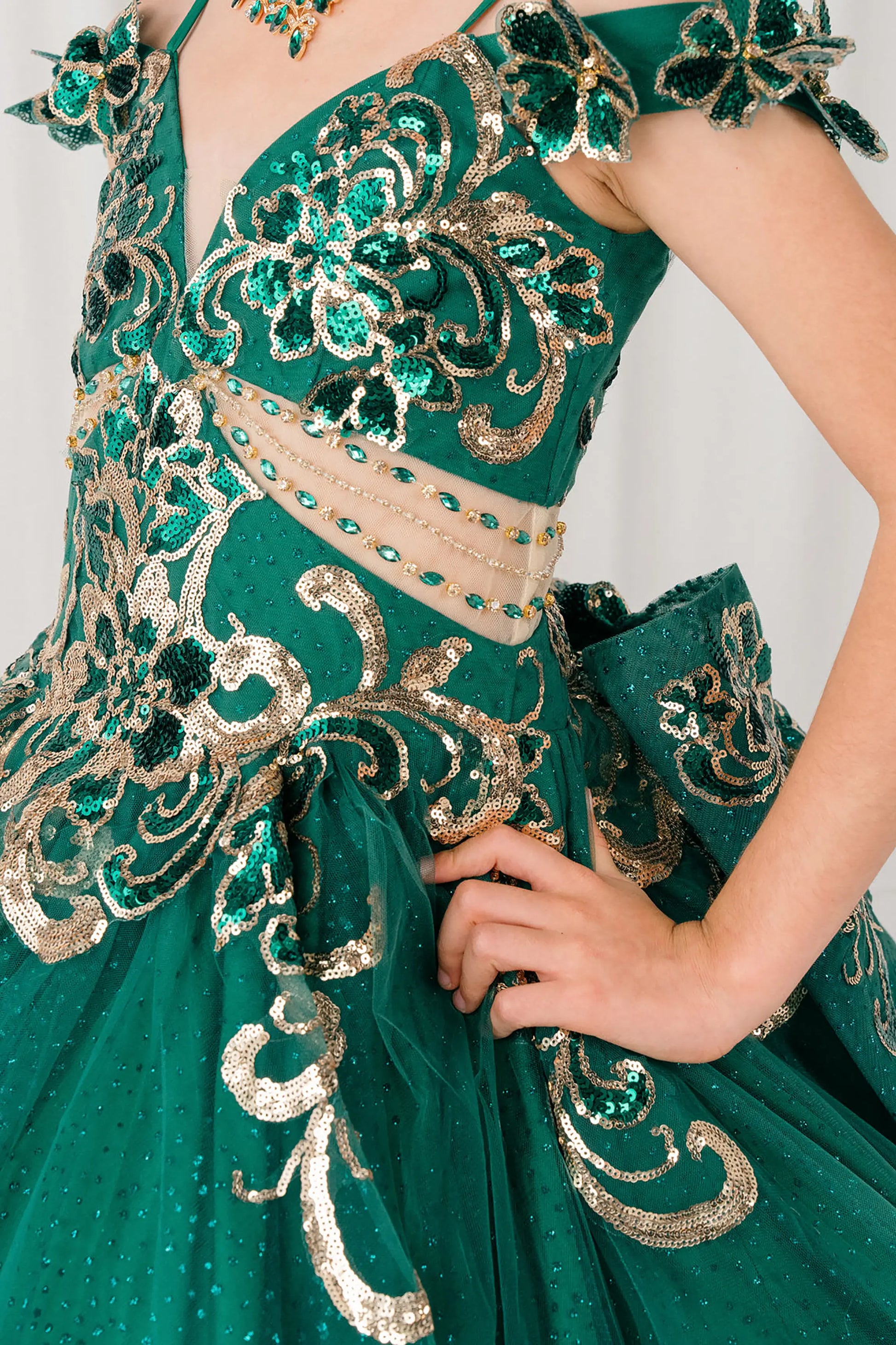 Side close up view of Hunter green mini quince ball gown with off shoulder floral embroidered bodice, glitter tulle skirt, lace up back, and layered bow