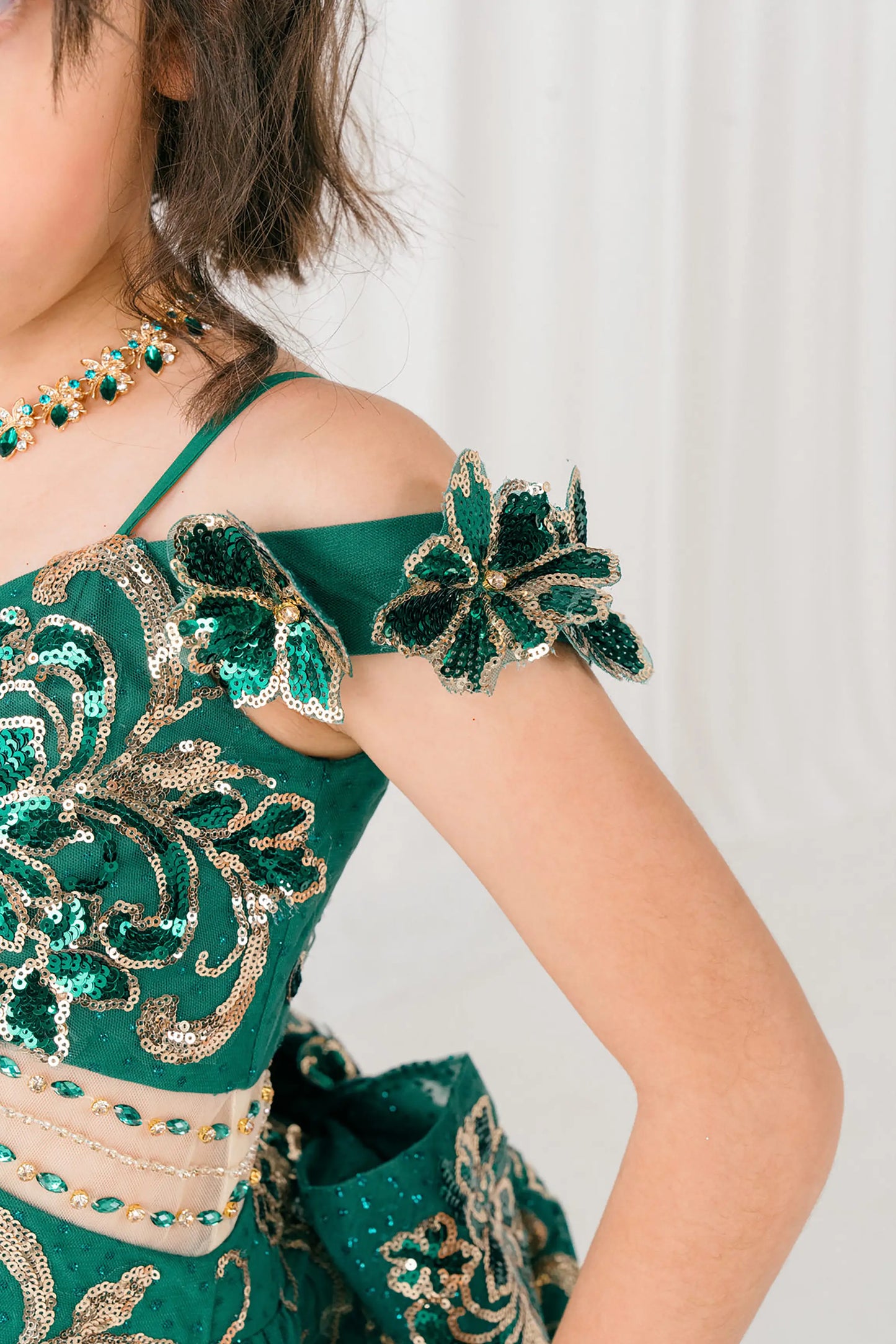Shoulder close up view of Hunter green mini quince ball gown with off shoulder floral embroidered bodice, glitter tulle skirt, lace up back, and layered bow